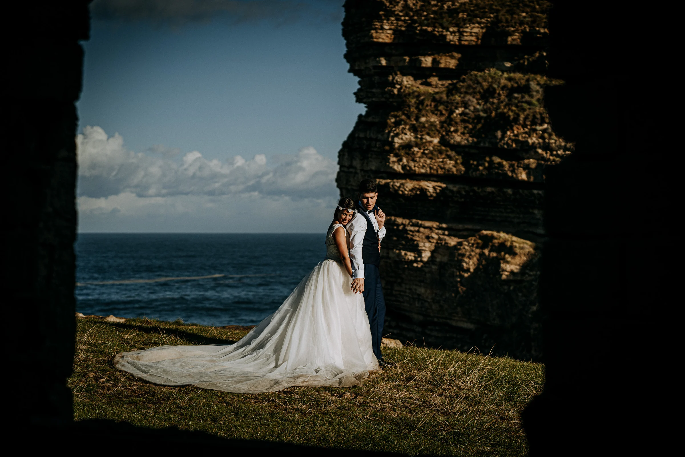 Pareja abrazada enmarcada por rocas frente al mar durante una sesión de postboda en El Molino, cerca de Llanes, Asturias.