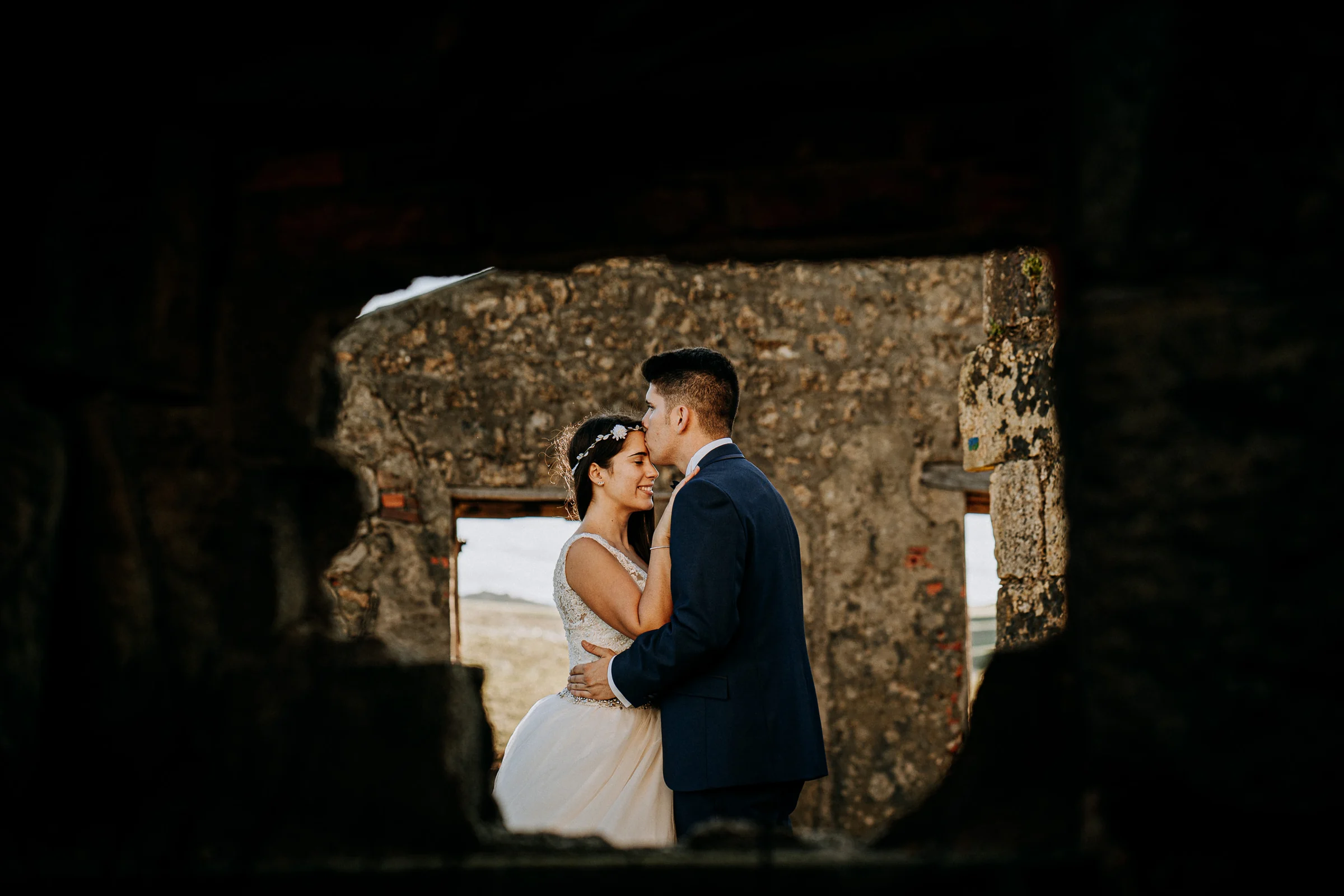 Pareja abrazada enmarcada por una abertura de piedra durante una sesión de postboda en El Molino, cerca de Llanes, Asturias.