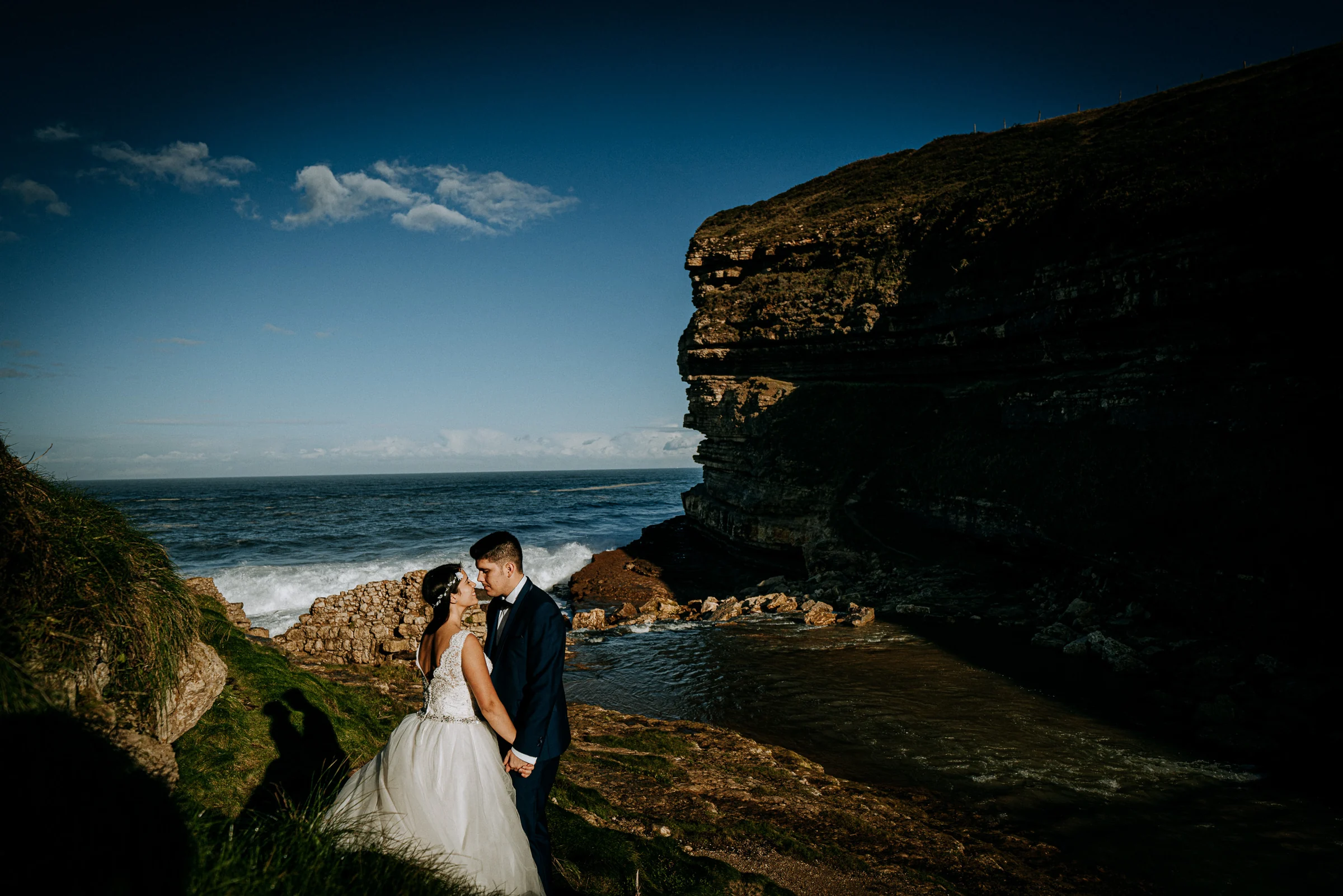 Pareja abrazada junto a un gran acantilado costero durante una sesión de postboda en El Molino, cerca de Llanes, Asturias.