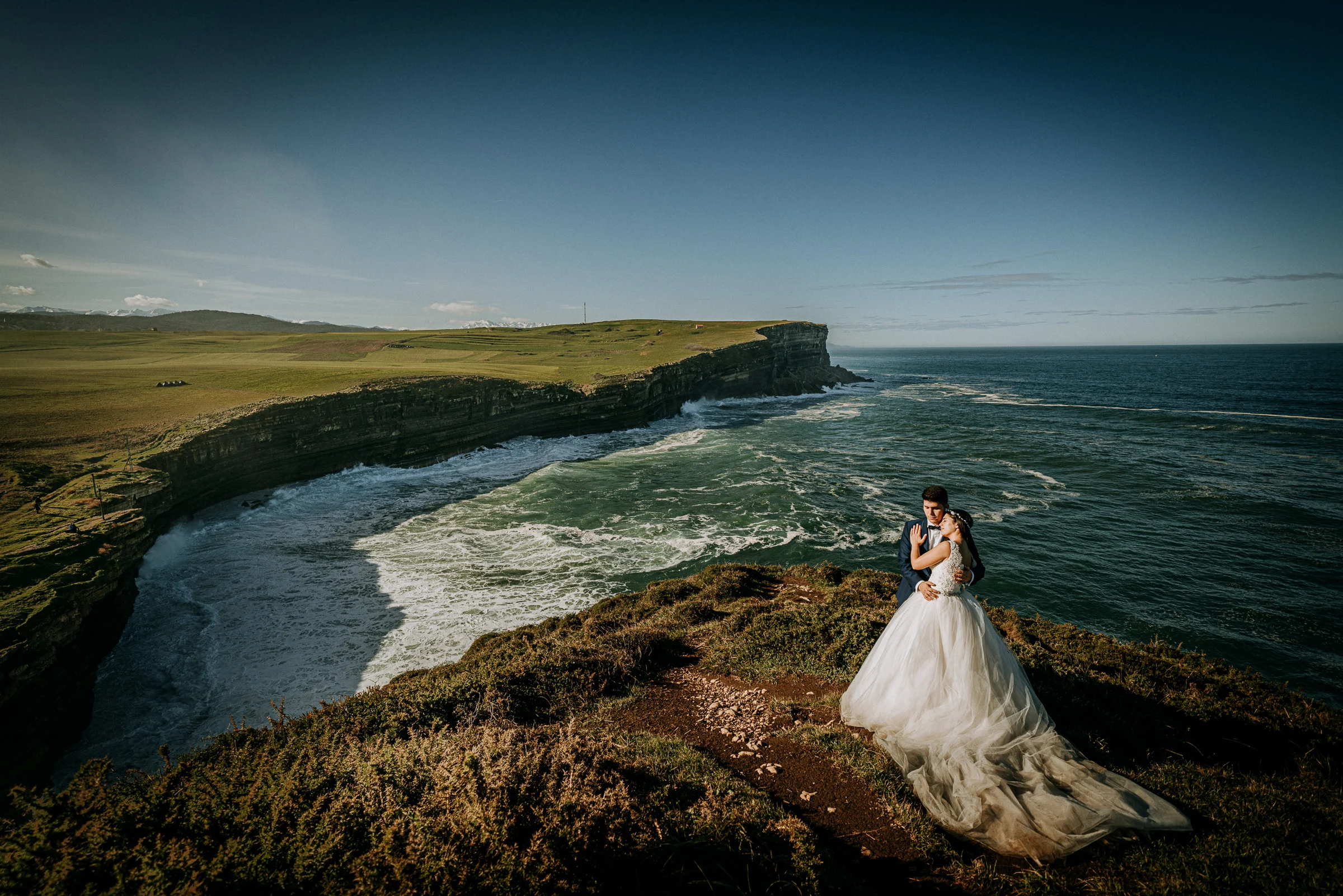 Pareja abrazada sobre un promontorio frente al mar durante una sesión de postboda en El Molino, cerca de Llanes, Asturias.