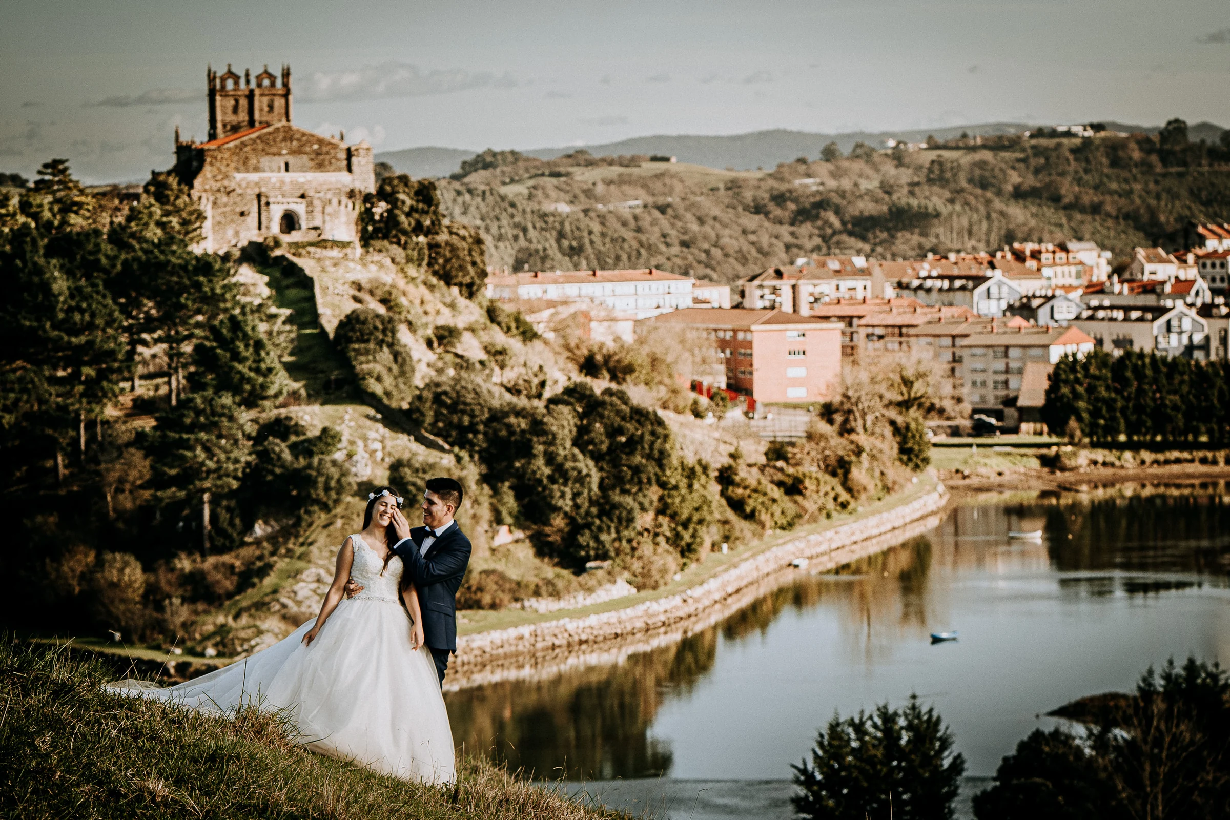 Pareja ante el estuario y el pueblo costero durante una sesión de postboda en El Molino, cerca de Llanes, Asturias.