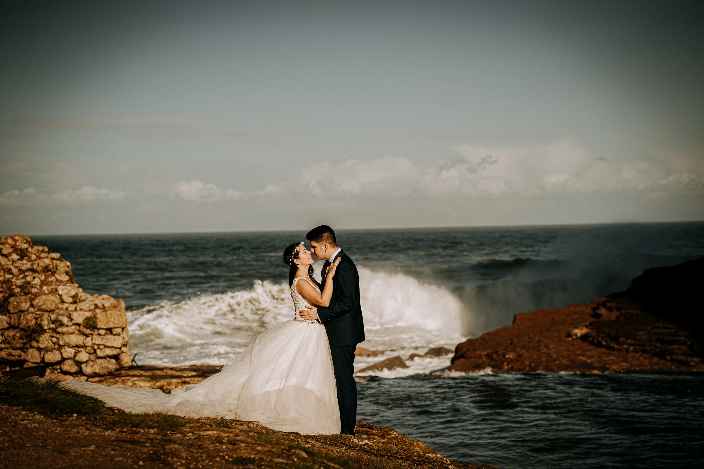 Pareja besándose con una gran ola rompiendo al fondo durante una sesión de postboda en El Molino, cerca de Llanes, Asturias.