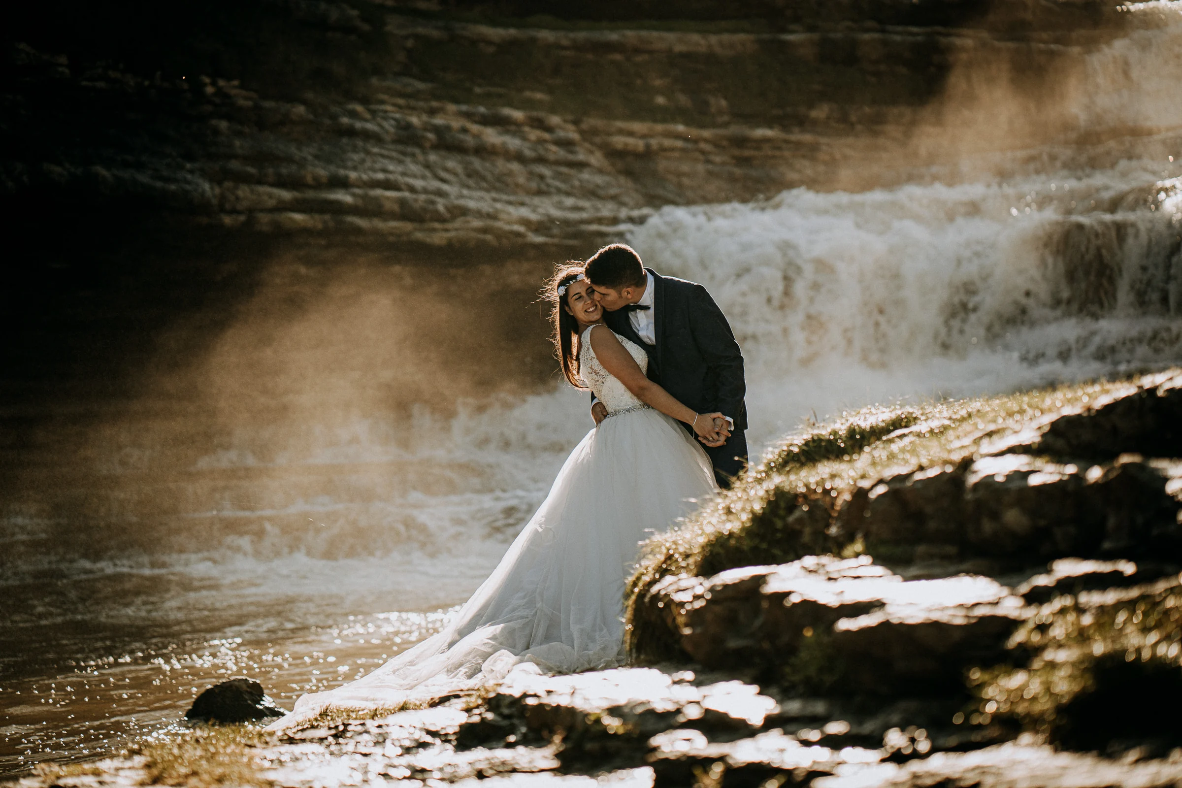 Pareja besándose junto a una cascada iluminada a contraluz durante una sesión de postboda en El Molino, cerca de Llanes, Asturias.