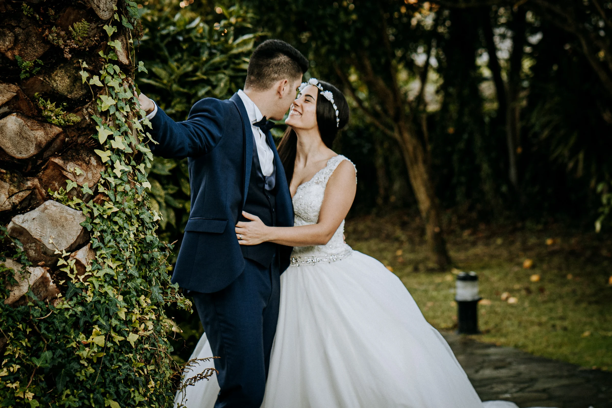 Pareja besándose junto a una palmera en el jardín durante una sesión de postboda en El Molino, cerca de Llanes, Asturias.