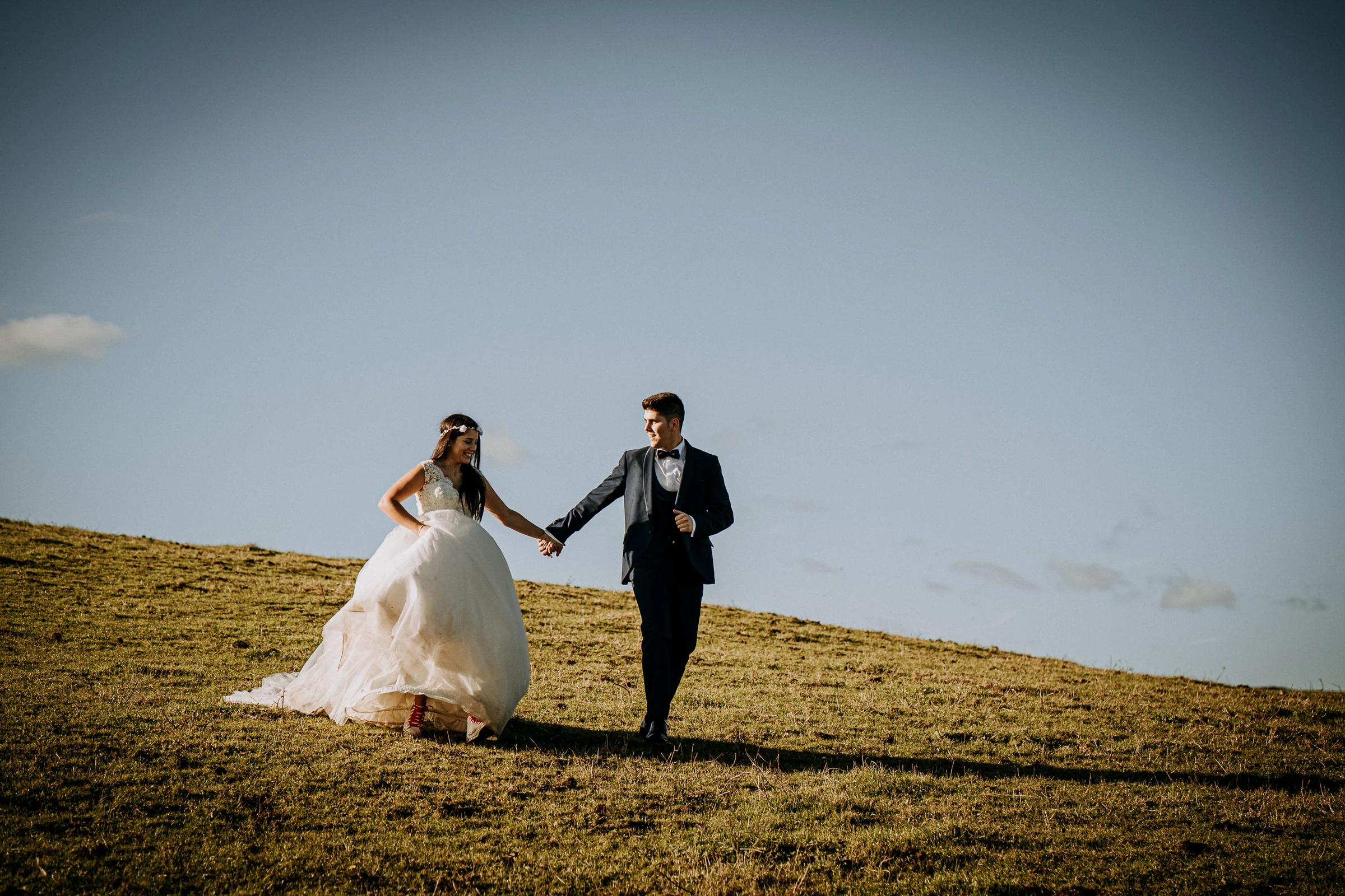 Pareja caminando de la mano por una ladera abierta durante una sesión de postboda en El Molino, cerca de Llanes, Asturias.