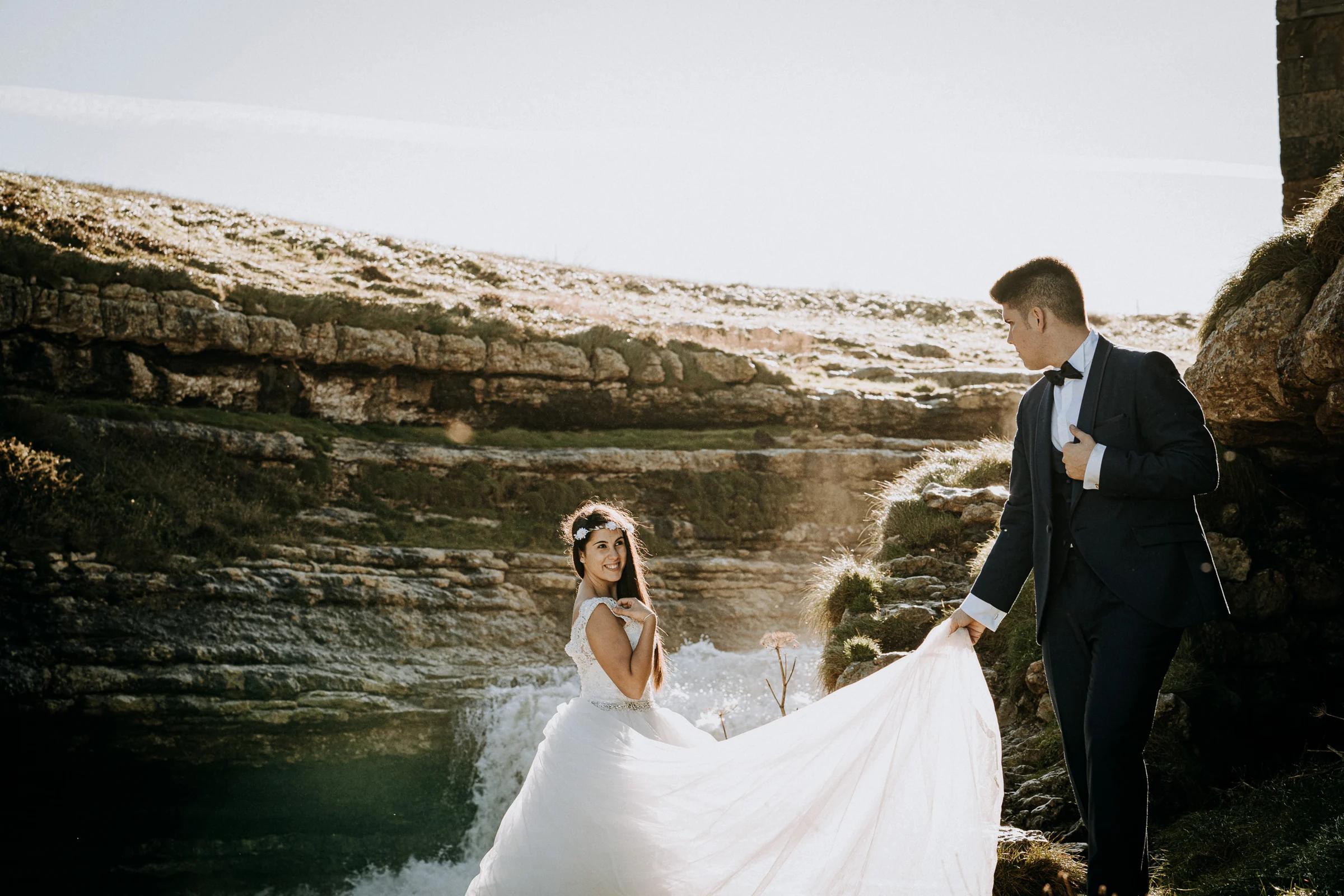 Pareja caminando junto a una cascada costera durante una sesión de postboda en El Molino, cerca de Llanes, Asturias.