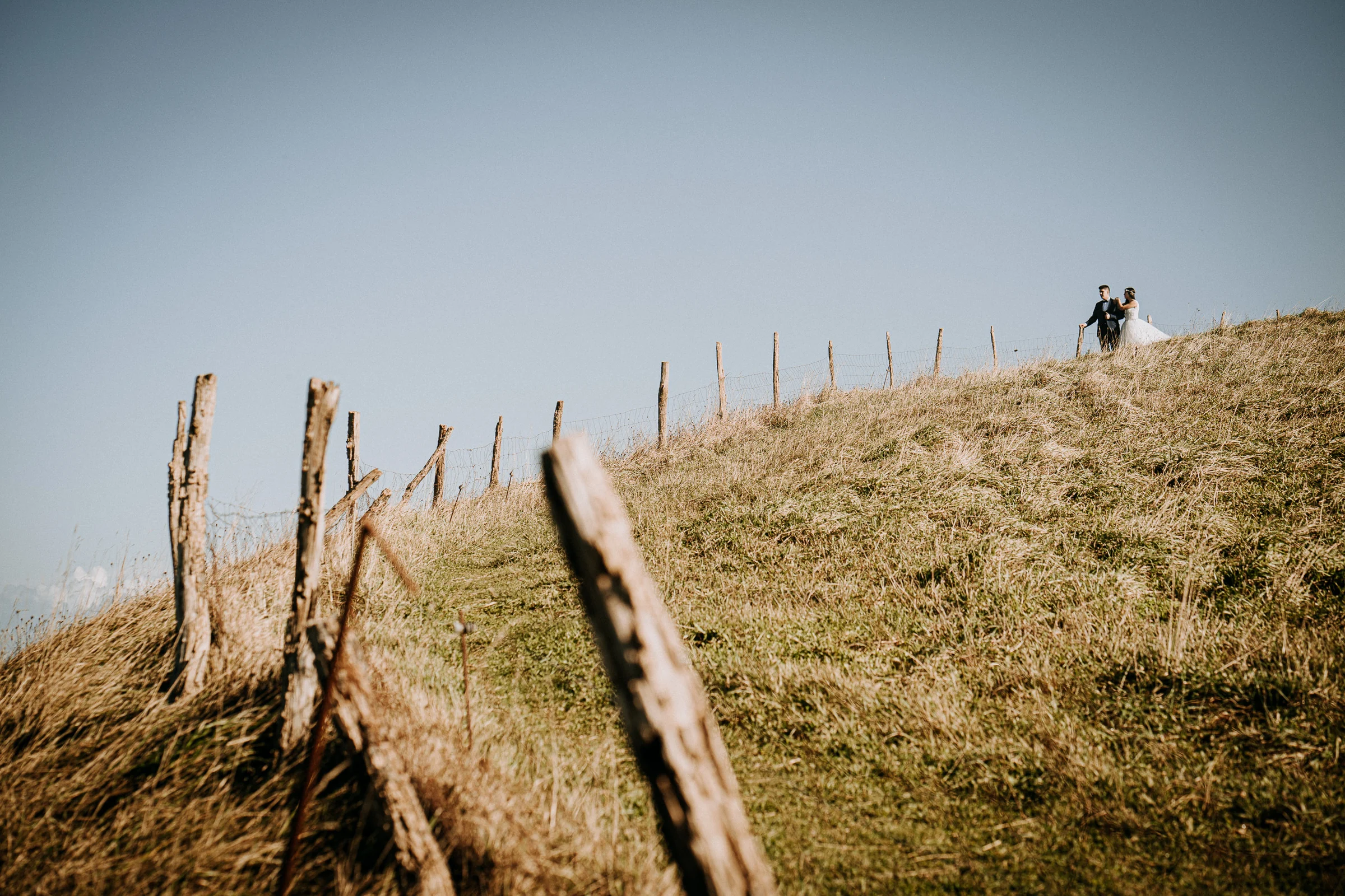 Pareja caminando por una ladera junto a una antigua valla durante una sesión de postboda en El Molino, cerca de Llanes, Asturias.