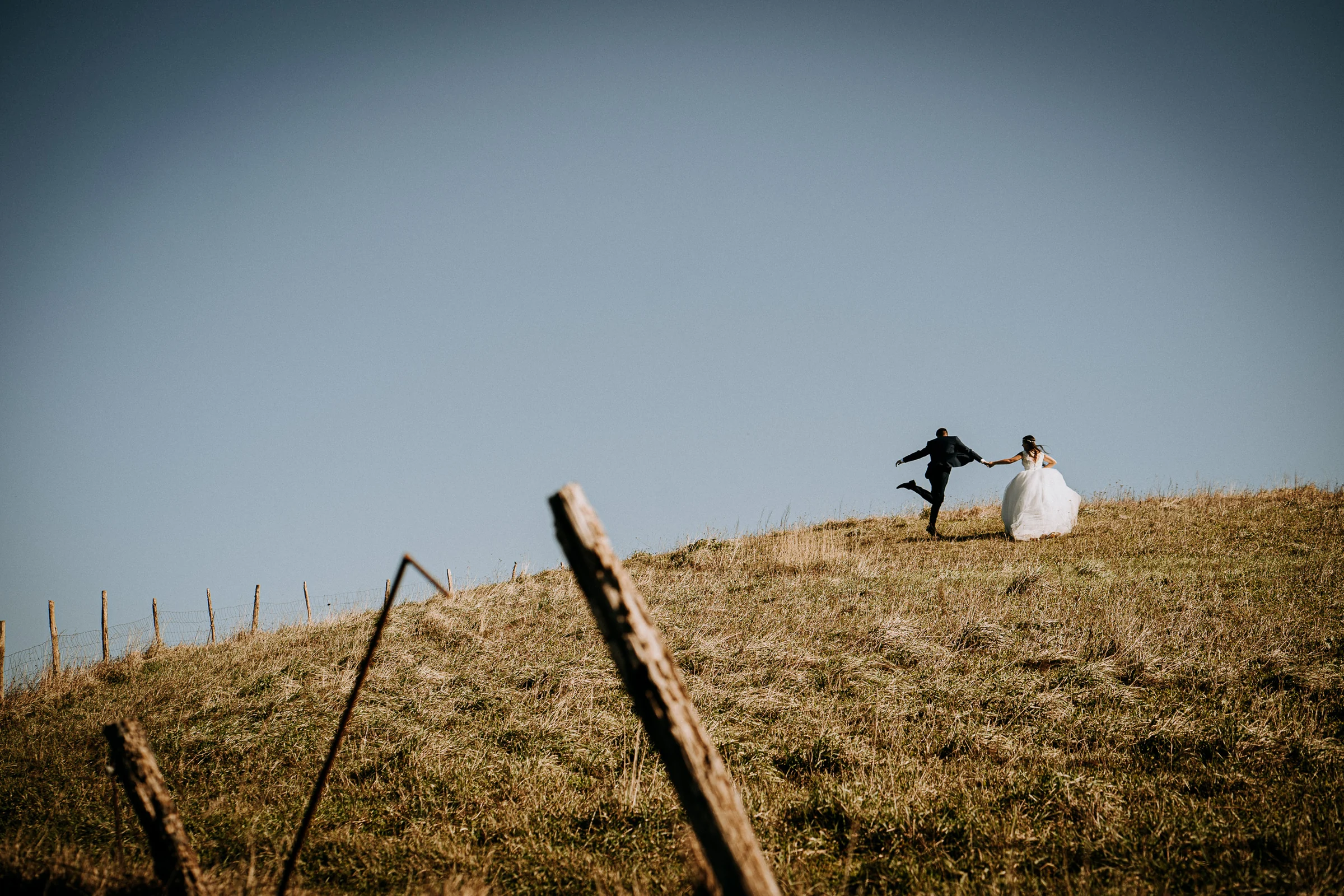 Pareja corriendo por la cresta de una colina costera durante una sesión de postboda en El Molino, cerca de Llanes, Asturias.