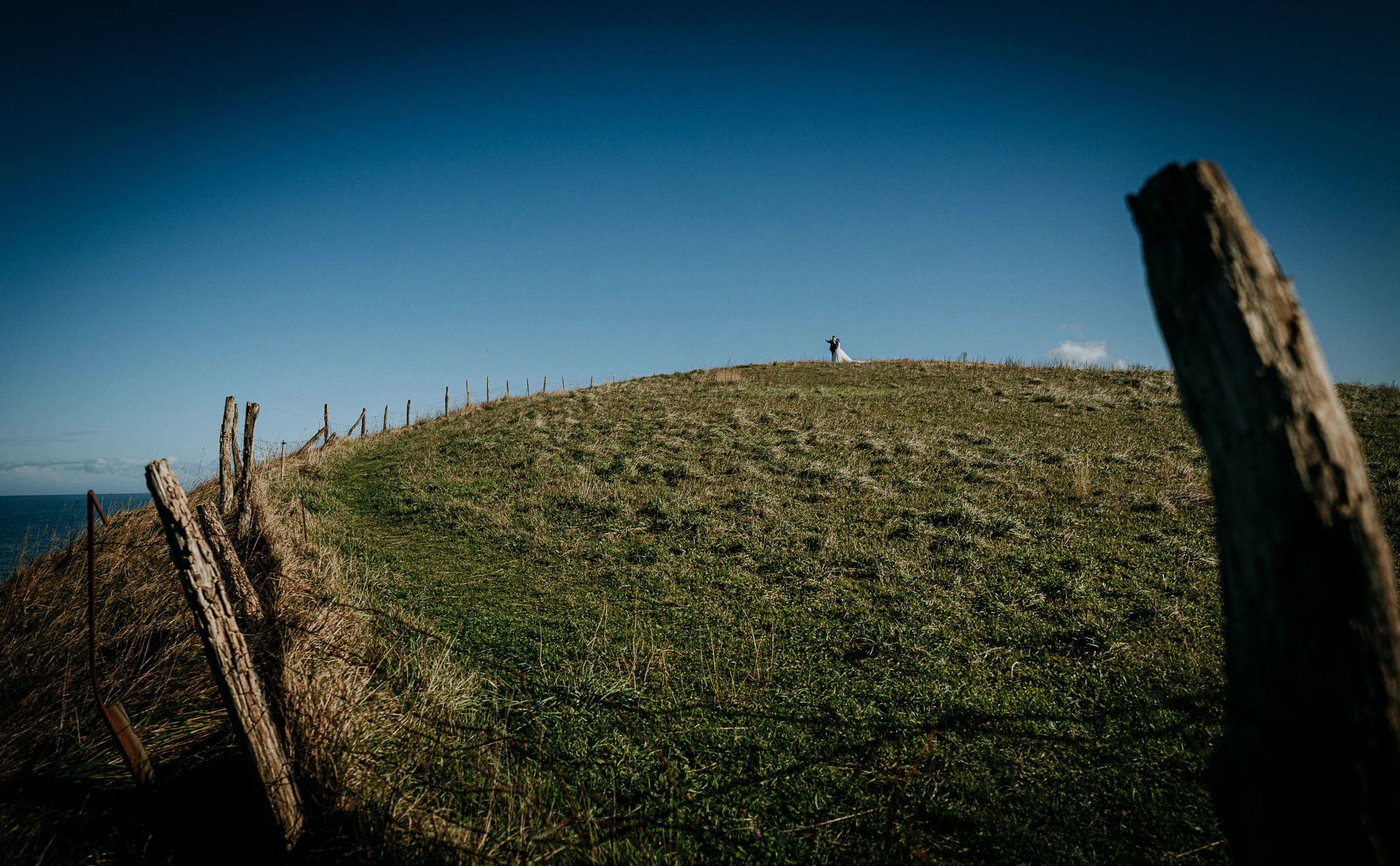 Pareja diminuta sobre una colina en un paisaje minimalista durante una sesión de postboda en El Molino, cerca de Llanes, Asturias.