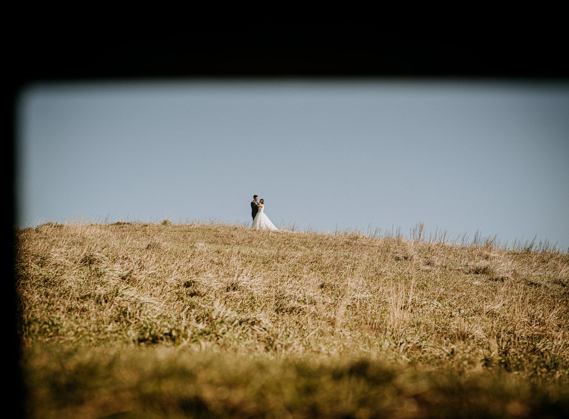 Pareja en la distancia sobre una colina frente al cielo durante una sesión de postboda en El Molino, cerca de Llanes, Asturias.