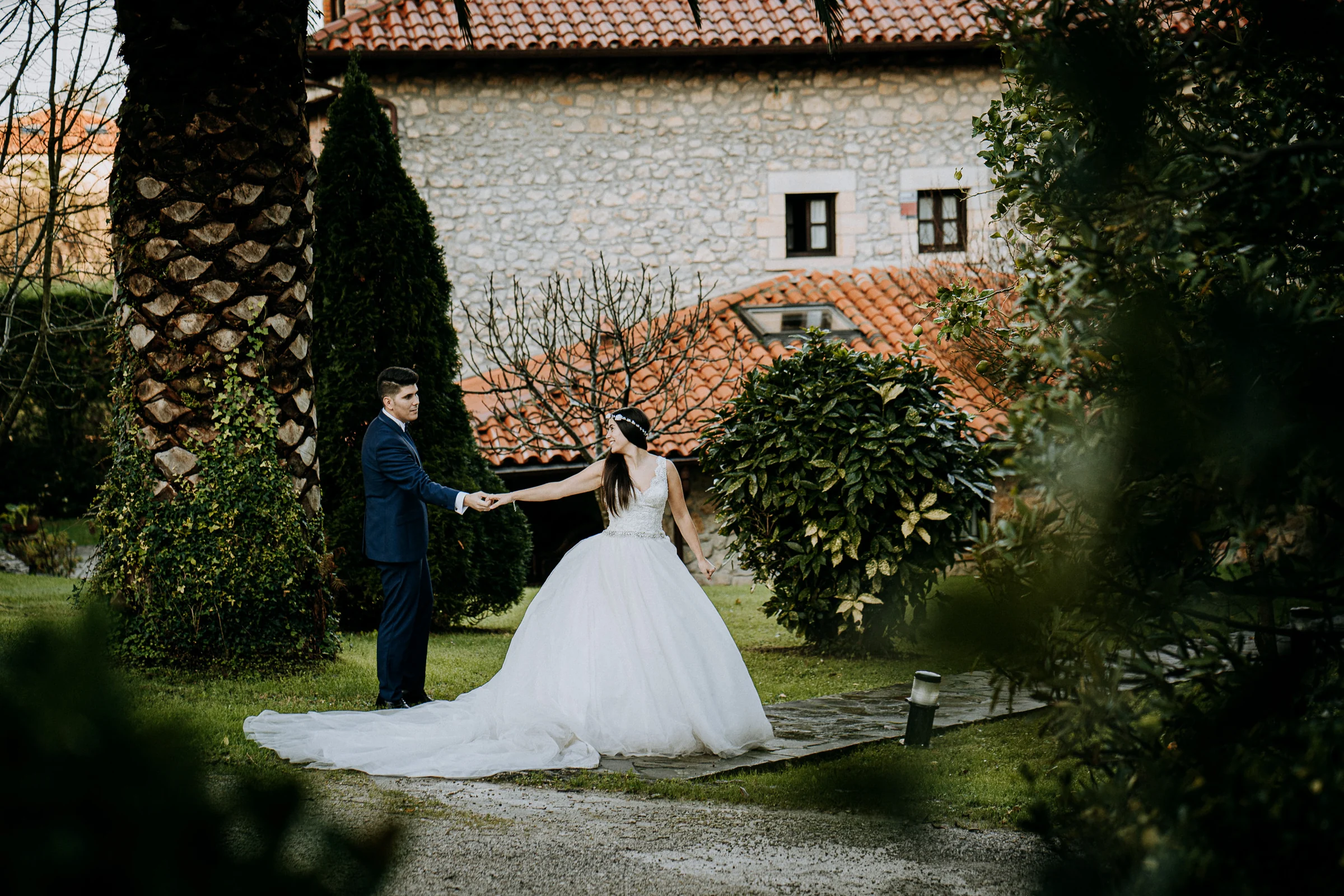 Pareja en un jardín junto a una casa de piedra durante una sesión de postboda en El Molino, cerca de Llanes, Asturias.