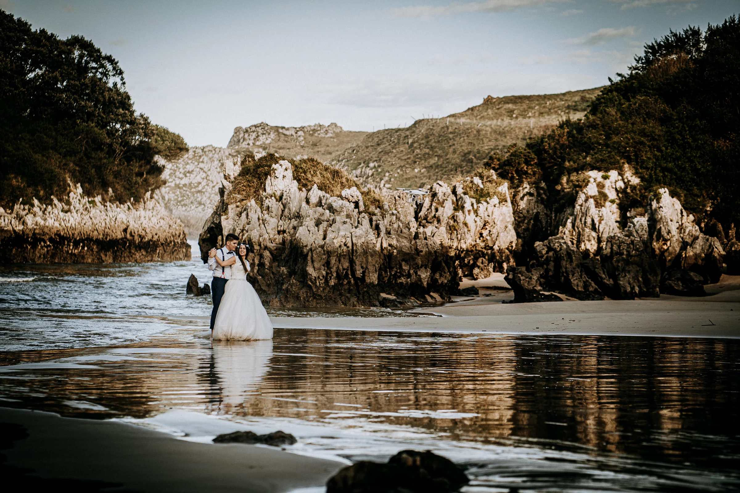 Pareja en una cala con reflejo sobre la arena mojada durante una sesión de postboda en El Molino, cerca de Llanes, Asturias.