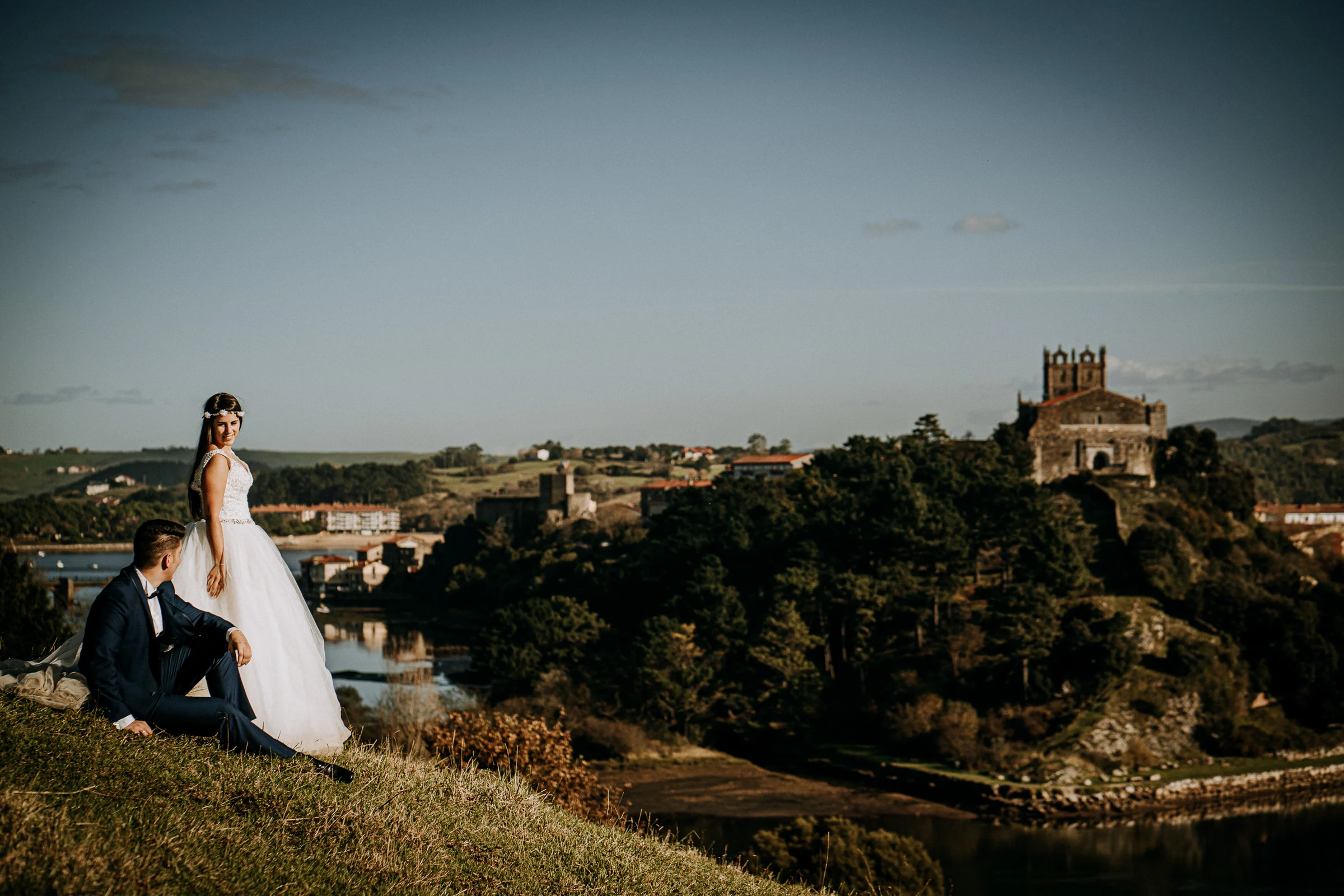 Pareja en una ladera con el estuario al fondo durante una sesión de postboda en El Molino, cerca de Llanes, Asturias.