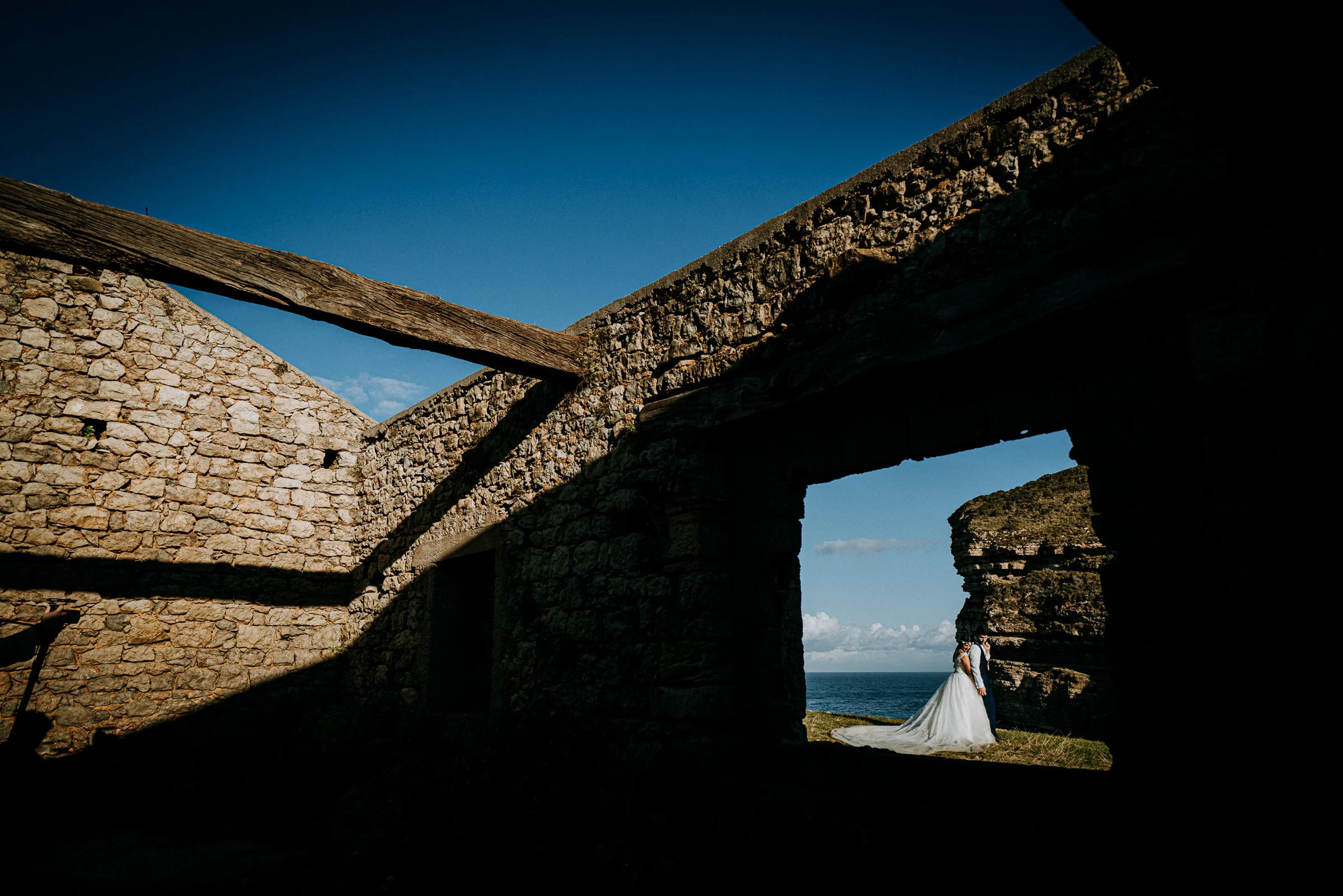 Pareja enmarcada por la arquitectura de unas ruinas durante una sesión de postboda en El Molino, cerca de Llanes, Asturias.