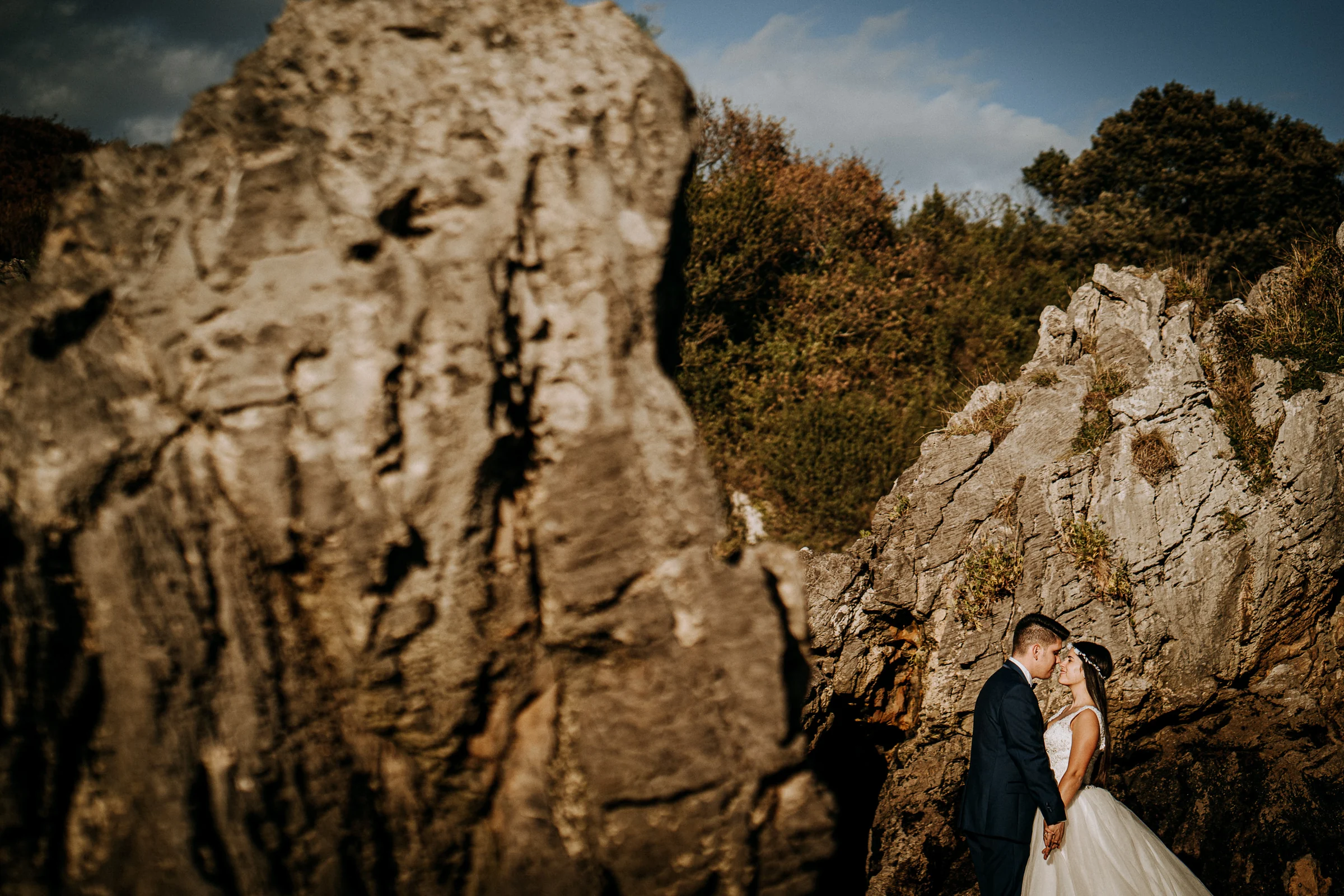 Pareja entre rocas con composición de profundidad durante una sesión de postboda en El Molino, cerca de Llanes, Asturias.