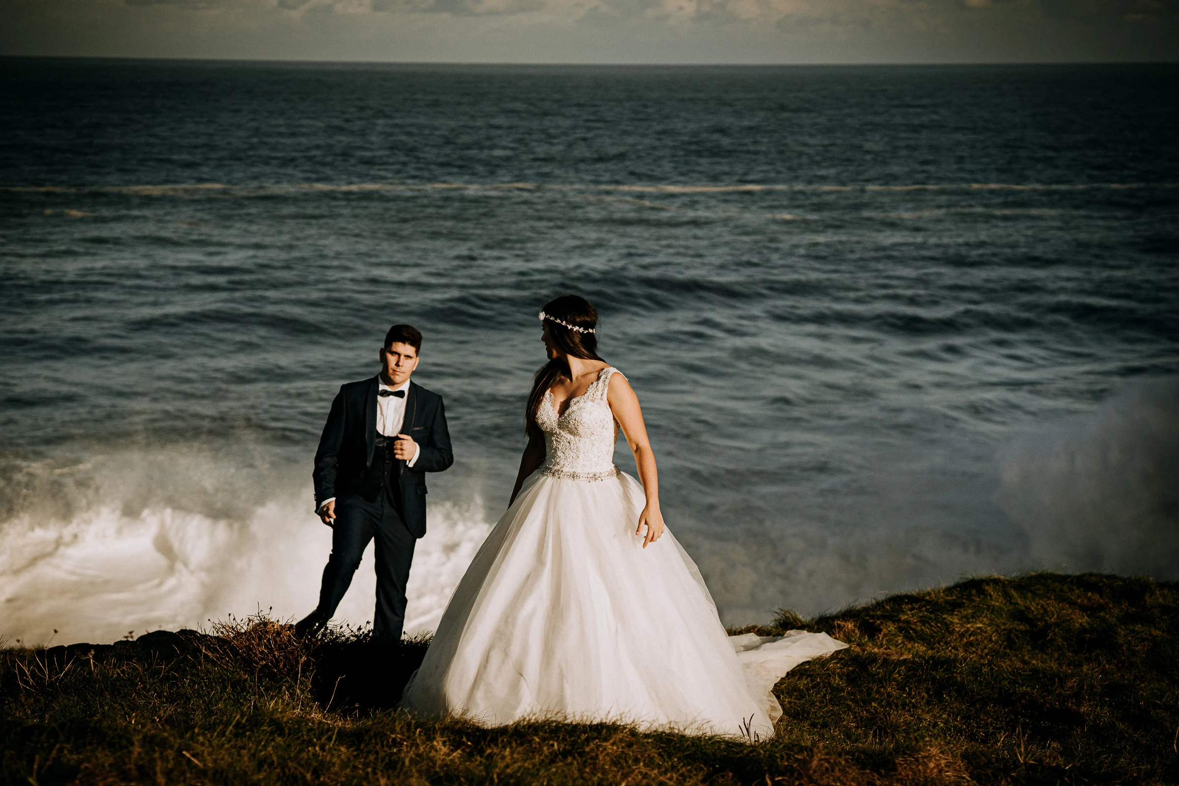 Pareja frente a un fuerte oleaje en la costa durante una sesión de postboda en El Molino, cerca de Llanes, Asturias.