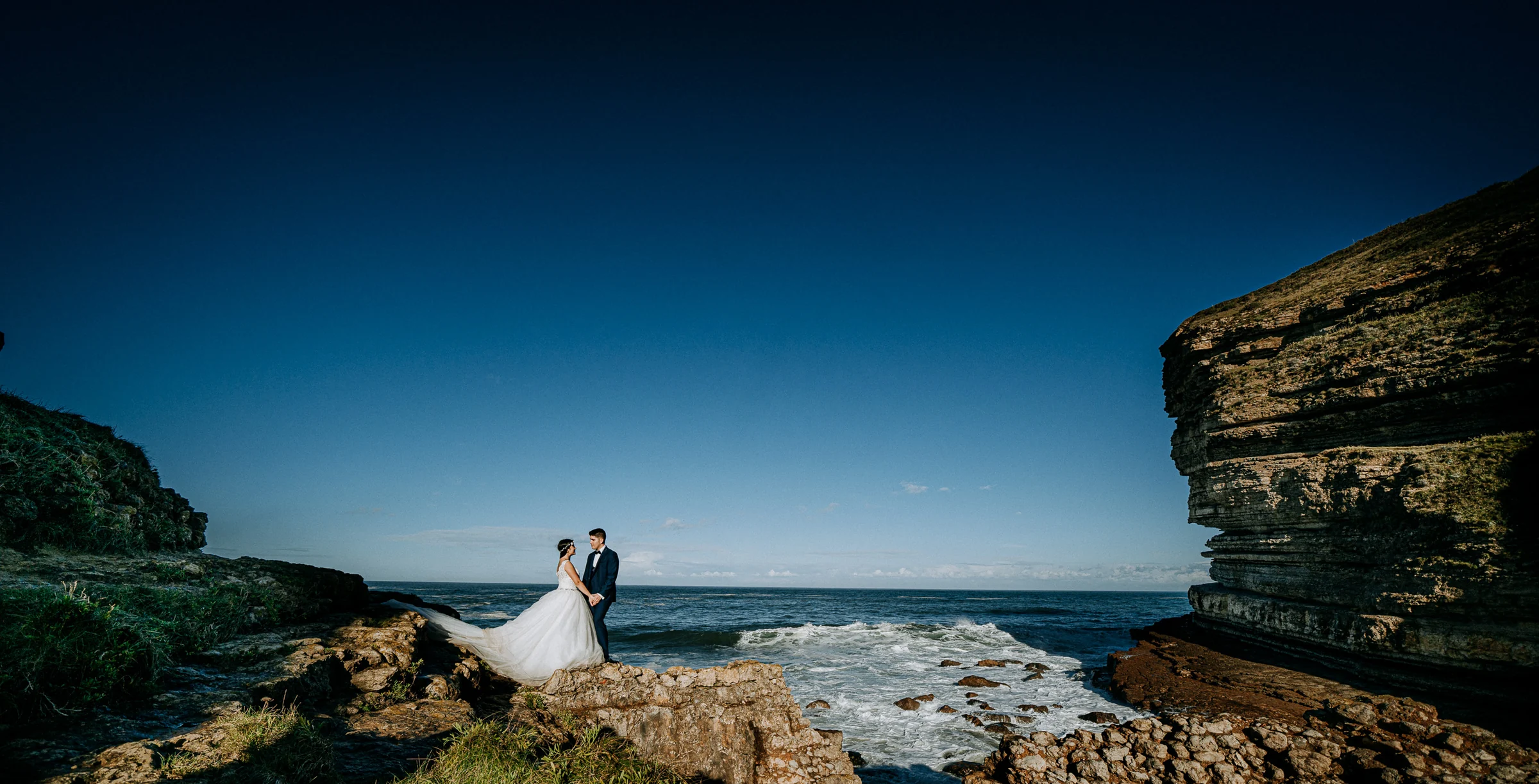 Pareja frente al océano entre grandes paredes de roca durante una sesión de postboda en El Molino, cerca de Llanes, Asturias.
