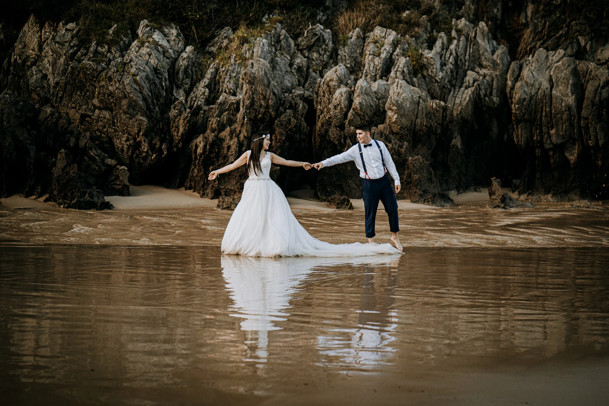 Pareja reflejada sobre la arena mojada durante una sesión de postboda en El Molino, cerca de Llanes, Asturias.