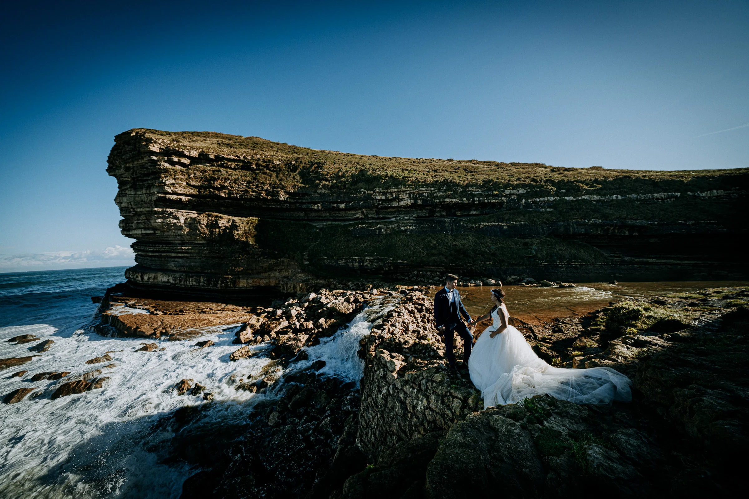 Pareja sobre las rocas con el acantilado y el mar de fondo durante una sesión de postboda en El Molino, cerca de Llanes, Asturias.