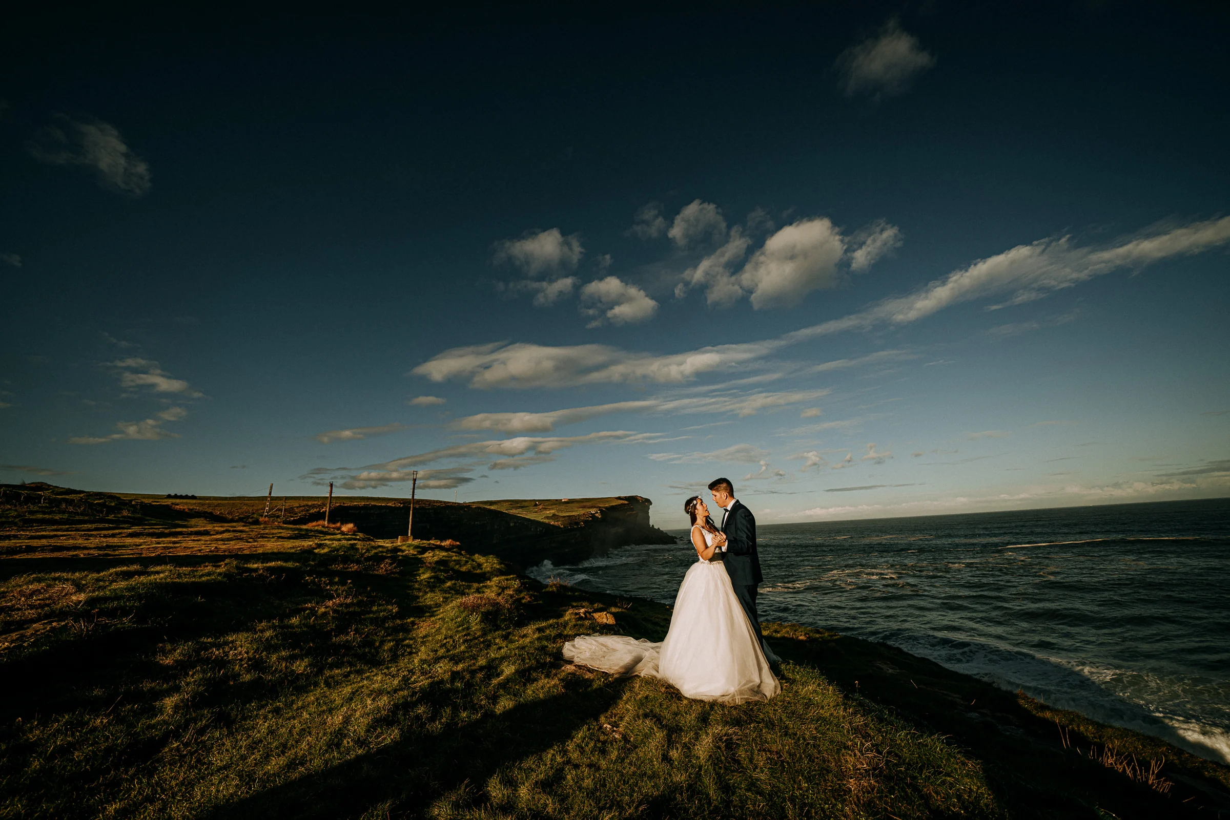 Pareja sobre un acantilado bajo un cielo dramático durante una sesión de postboda en El Molino, cerca de Llanes, Asturias.