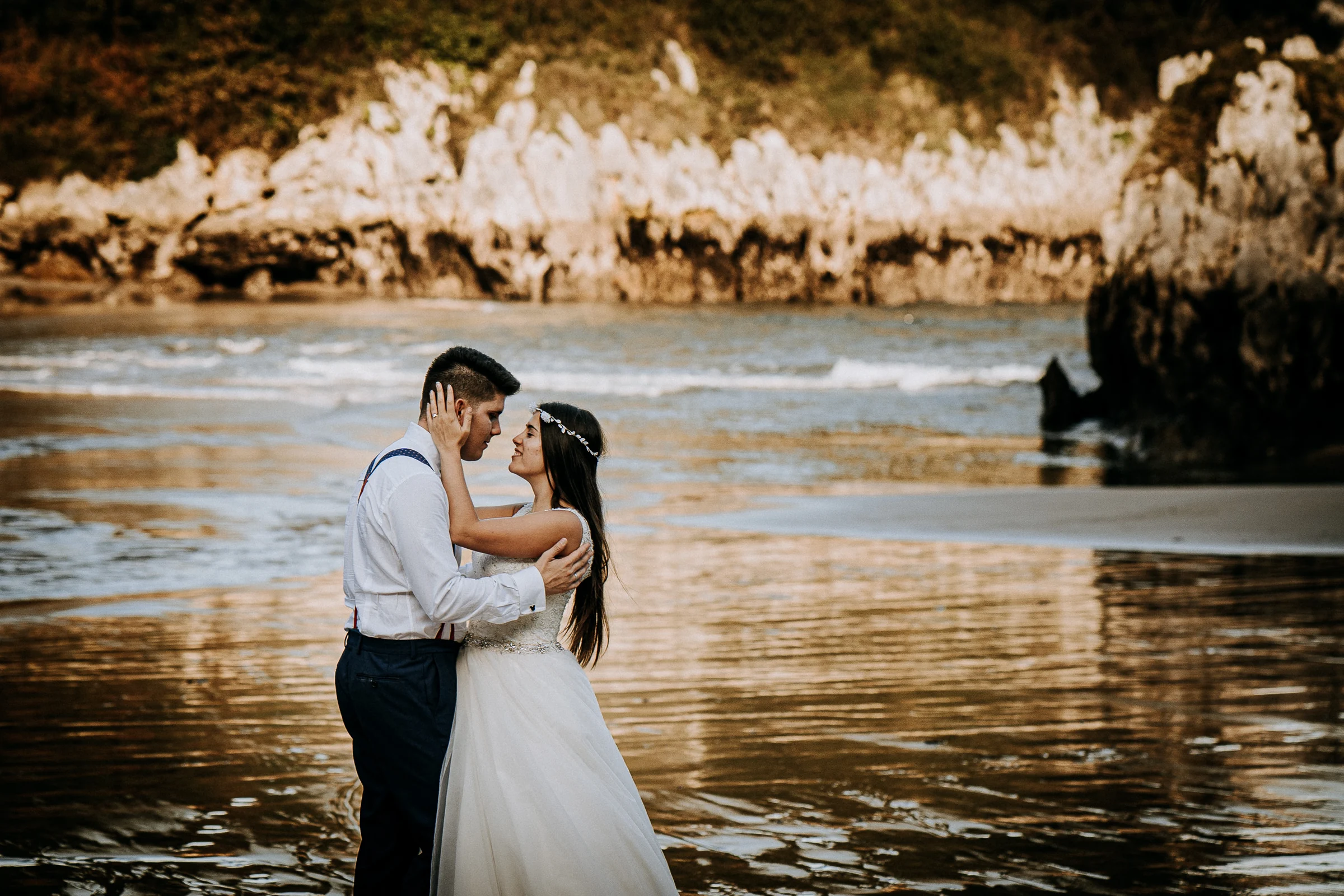 Retrato cercano de la pareja abrazada en la playa durante una sesión de postboda en El Molino, cerca de Llanes, Asturias.