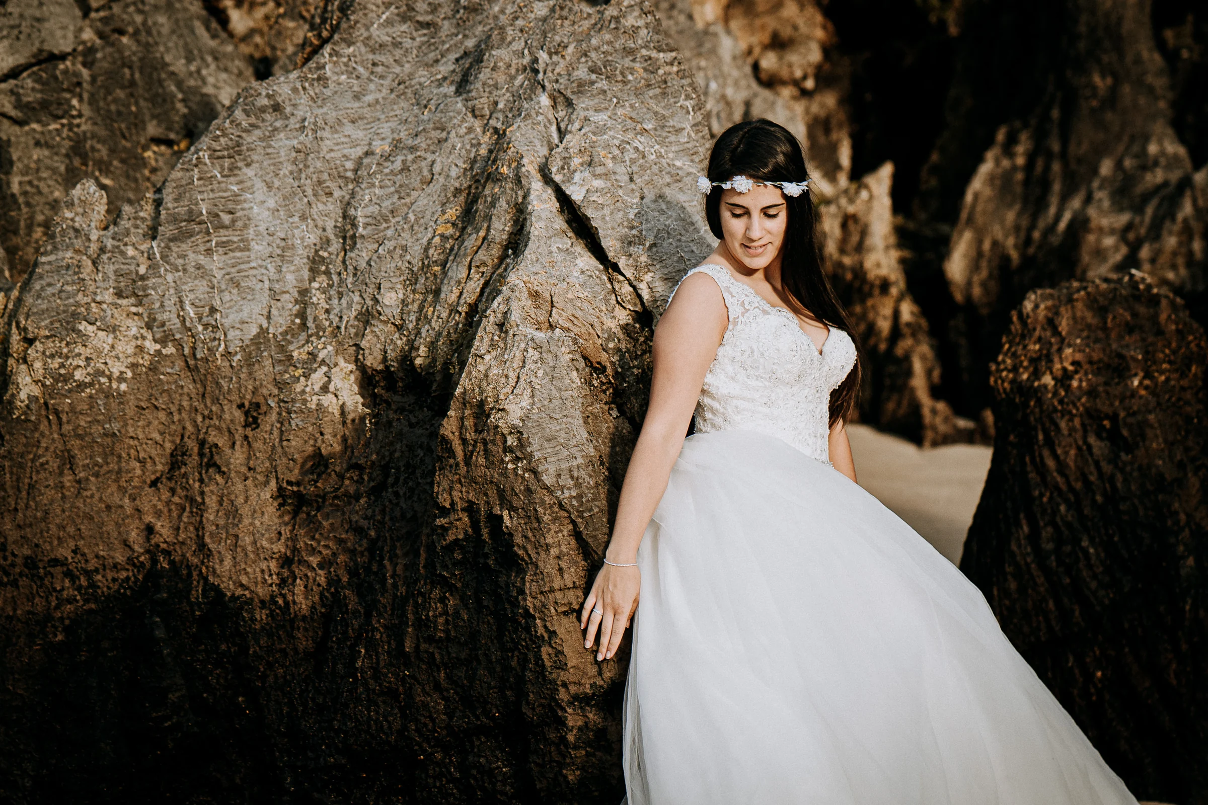 Retrato de la novia entre grandes rocas costeras durante una sesión de postboda en El Molino, cerca de Llanes, Asturias.