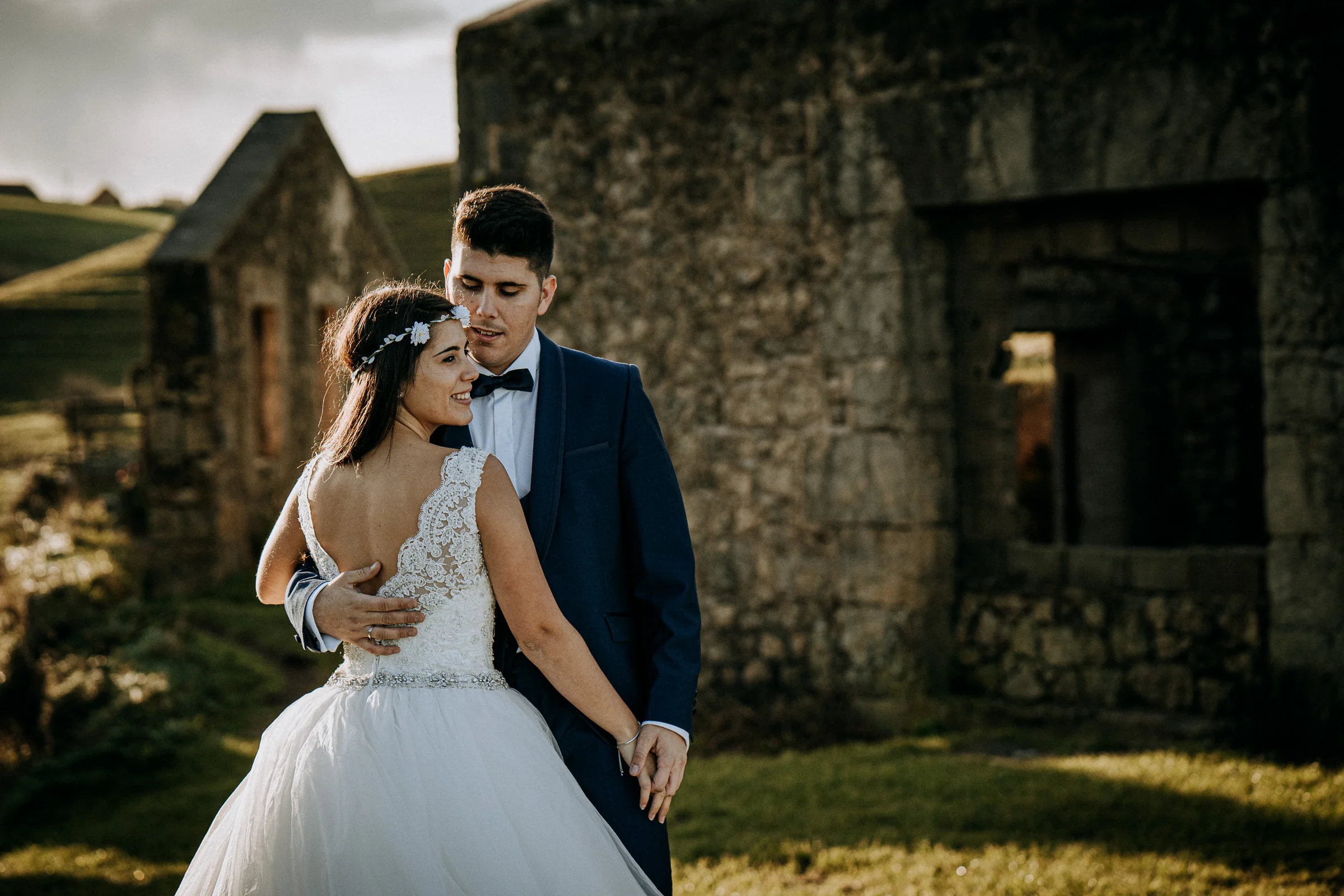 Retrato de la pareja junto a unas antiguas construcciones de piedra durante una sesión de postboda en El Molino, cerca de Llanes, Asturias.