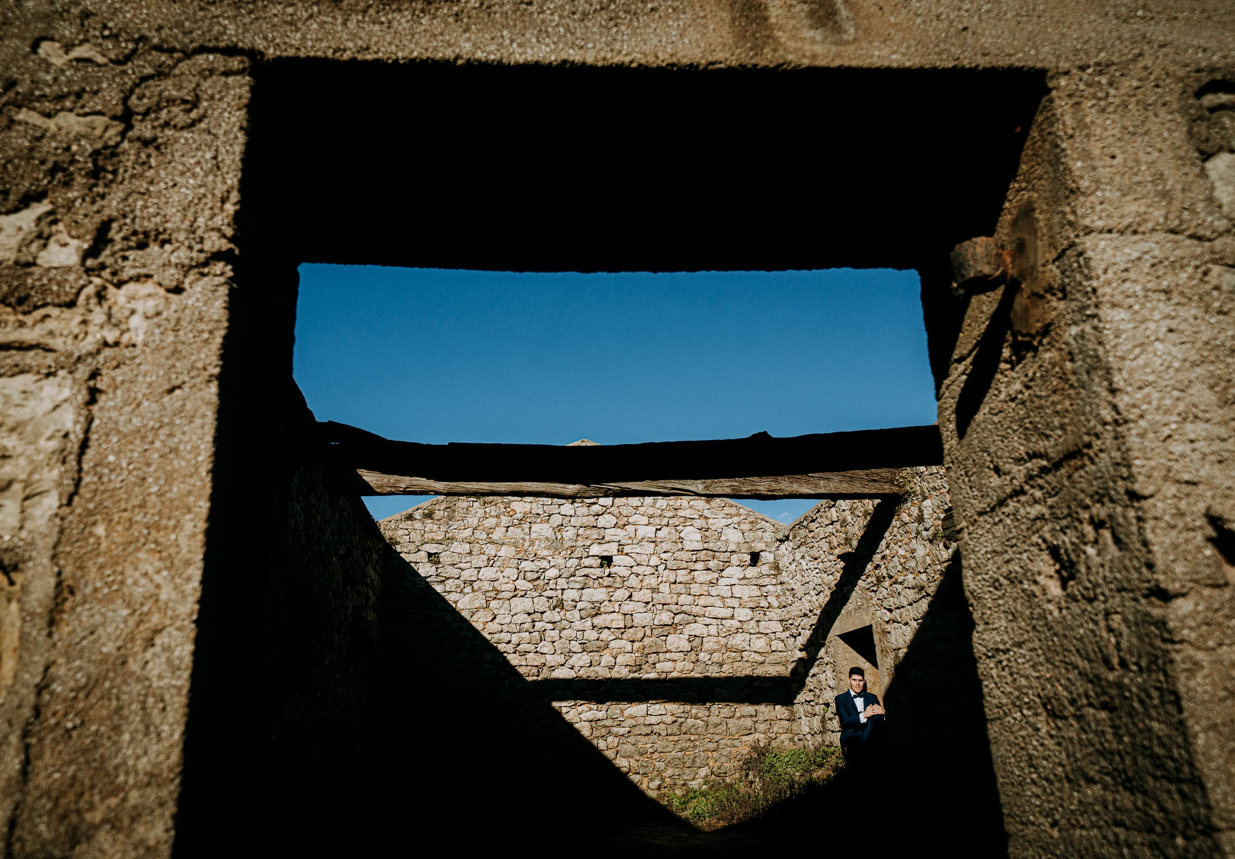 Retrato del novio enmarcado por una ventana de piedra durante una sesión de postboda en El Molino, cerca de Llanes, Asturias.