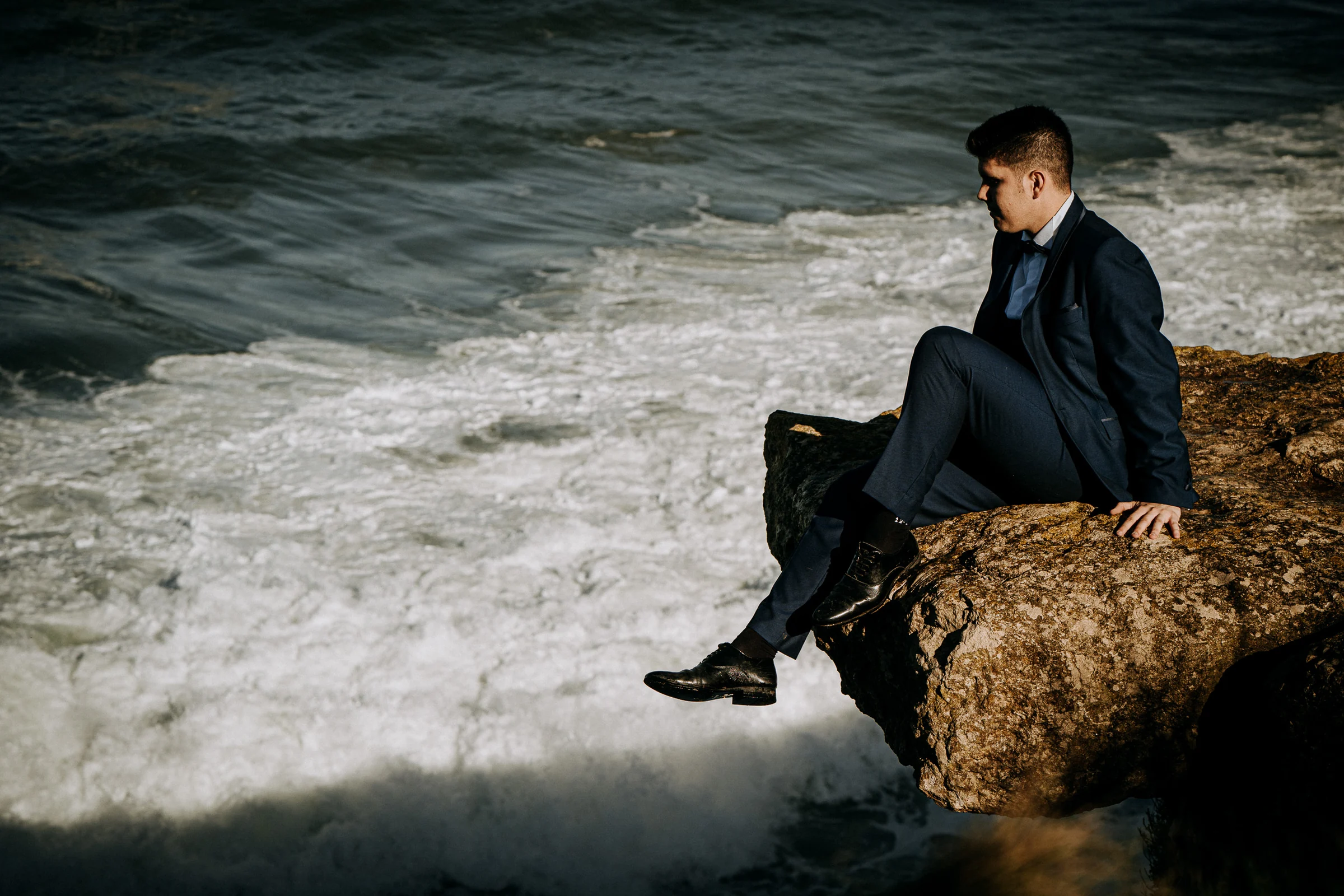 Retrato del novio sentado sobre las rocas frente al mar durante una sesión de postboda en El Molino, cerca de Llanes, Asturias.