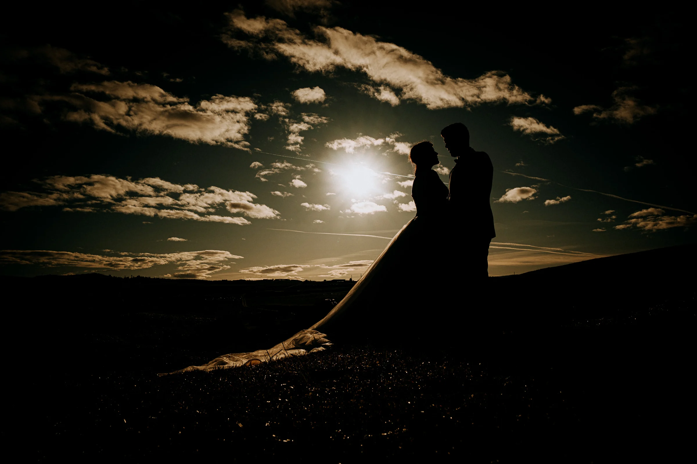 Silueta de la pareja frente al sol y un cielo de nubes durante una sesión de postboda en El Molino, cerca de Llanes, Asturias.