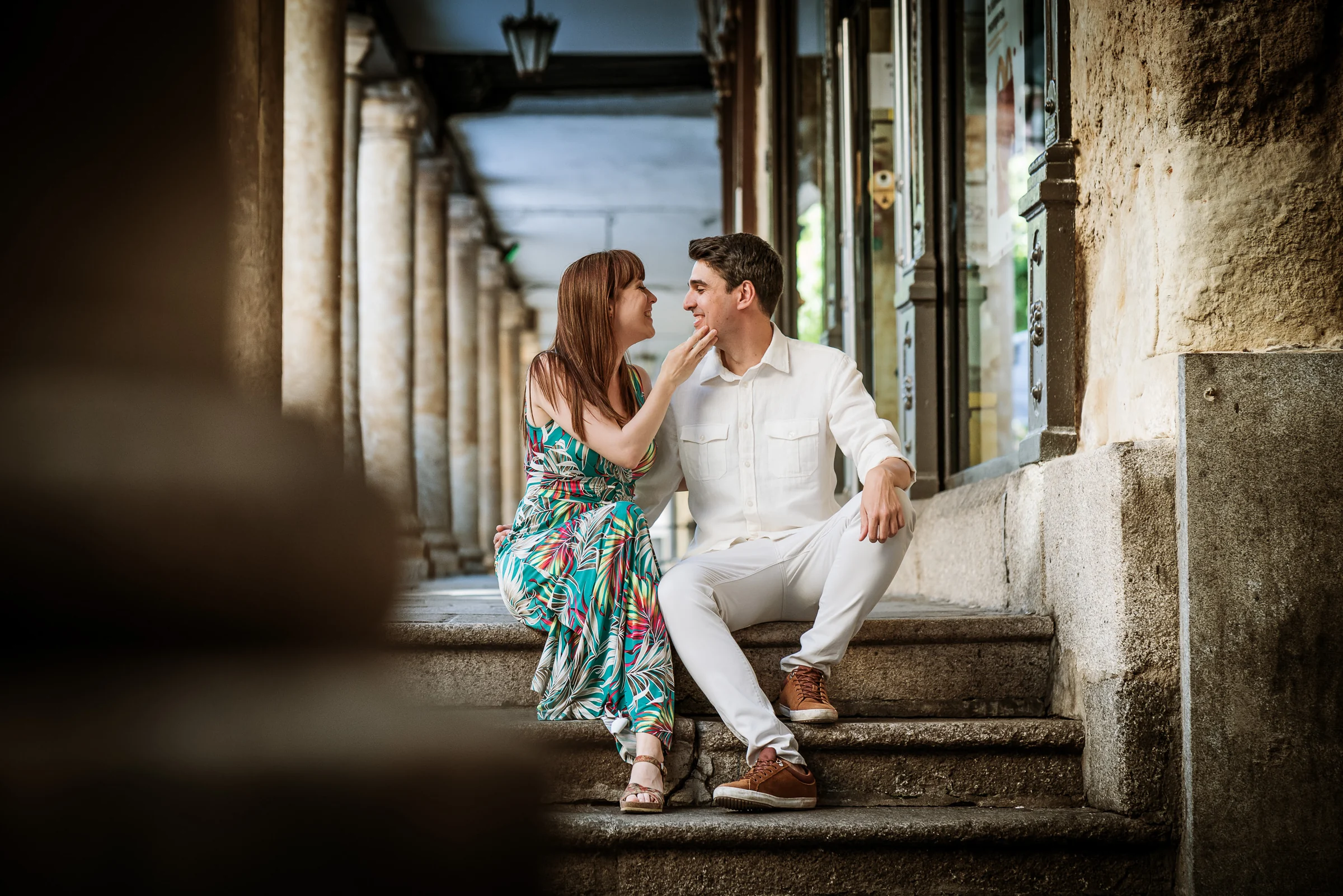 David y Noelia conversan sentados bajo los soportales de una calle histórica de Salamanca.