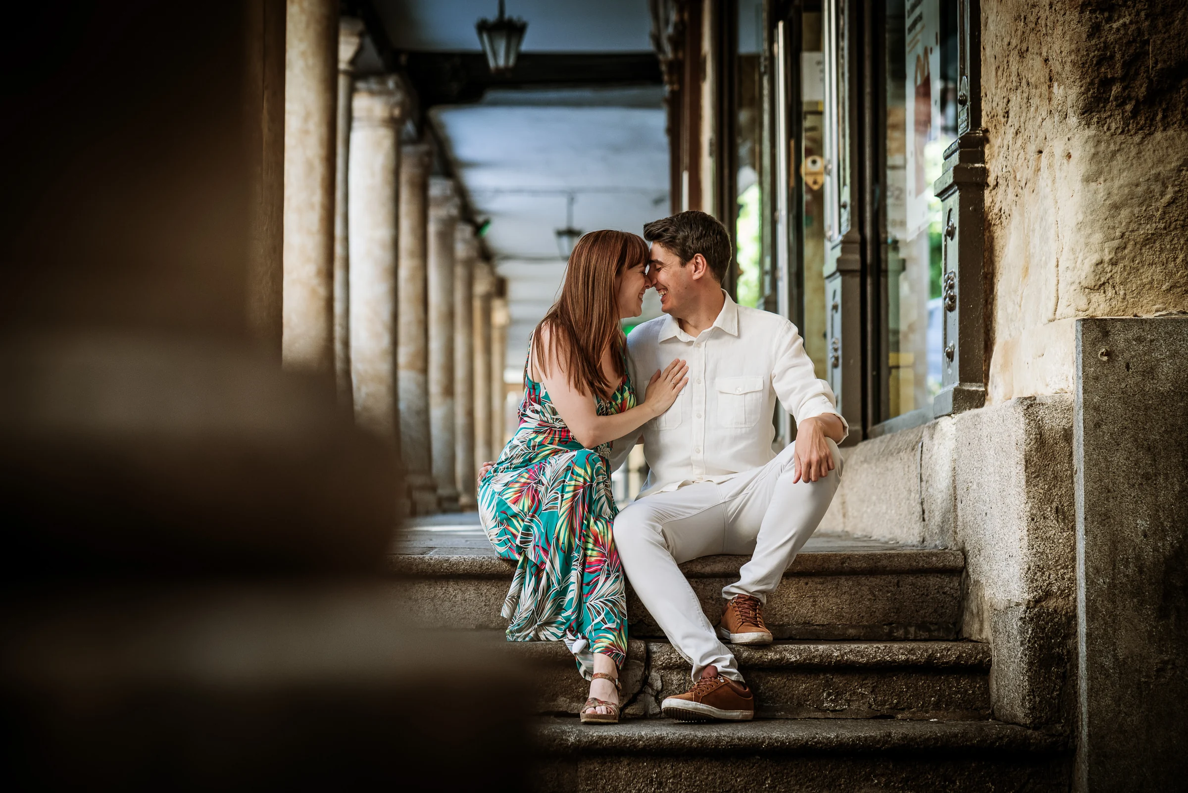 David y Noelia se miran sentados bajo los soportales de piedra durante su preboda en Salamanca.
