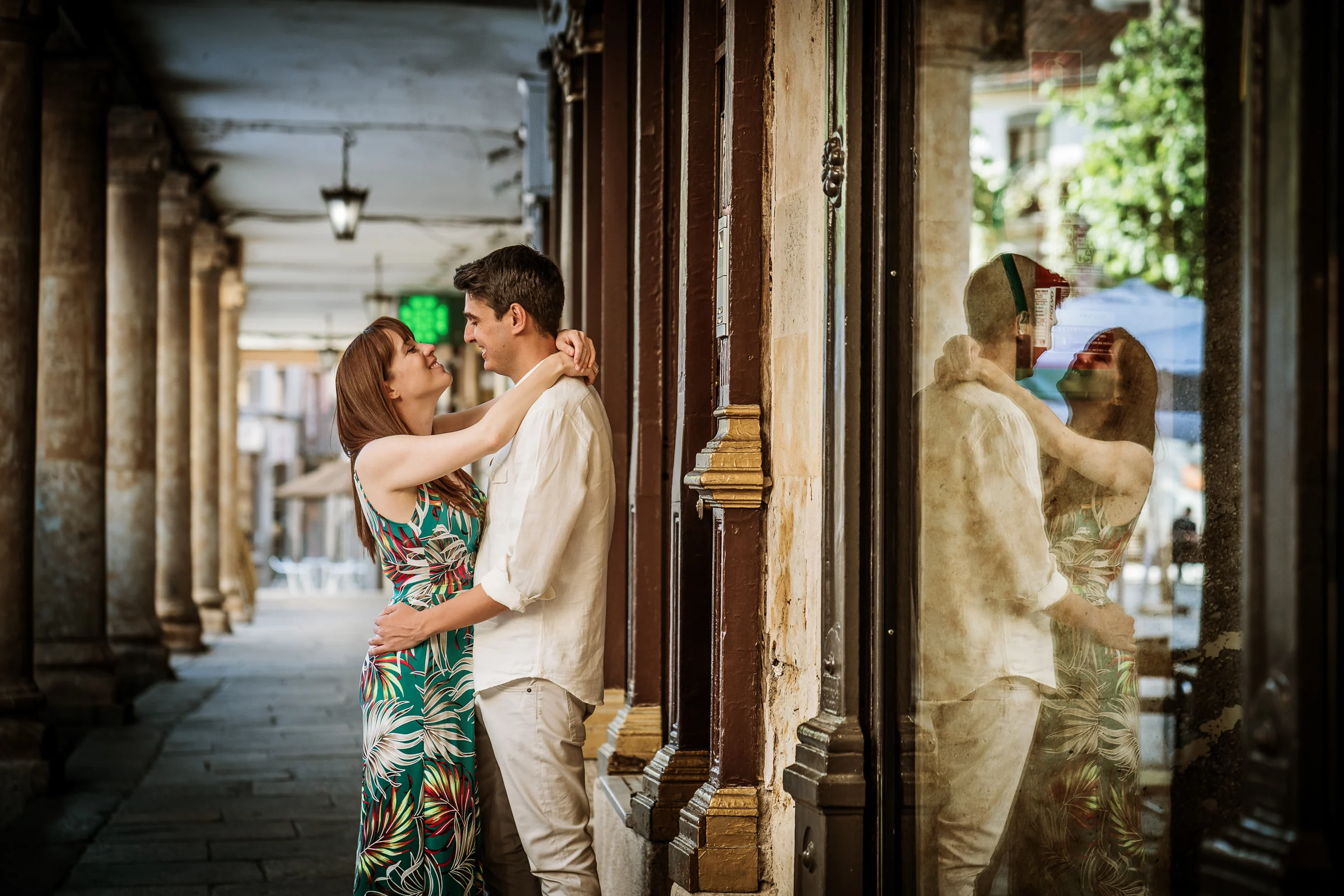 David y Noelia se abrazan junto a un escaparate que refleja los soportales del centro histórico de Salamanca.