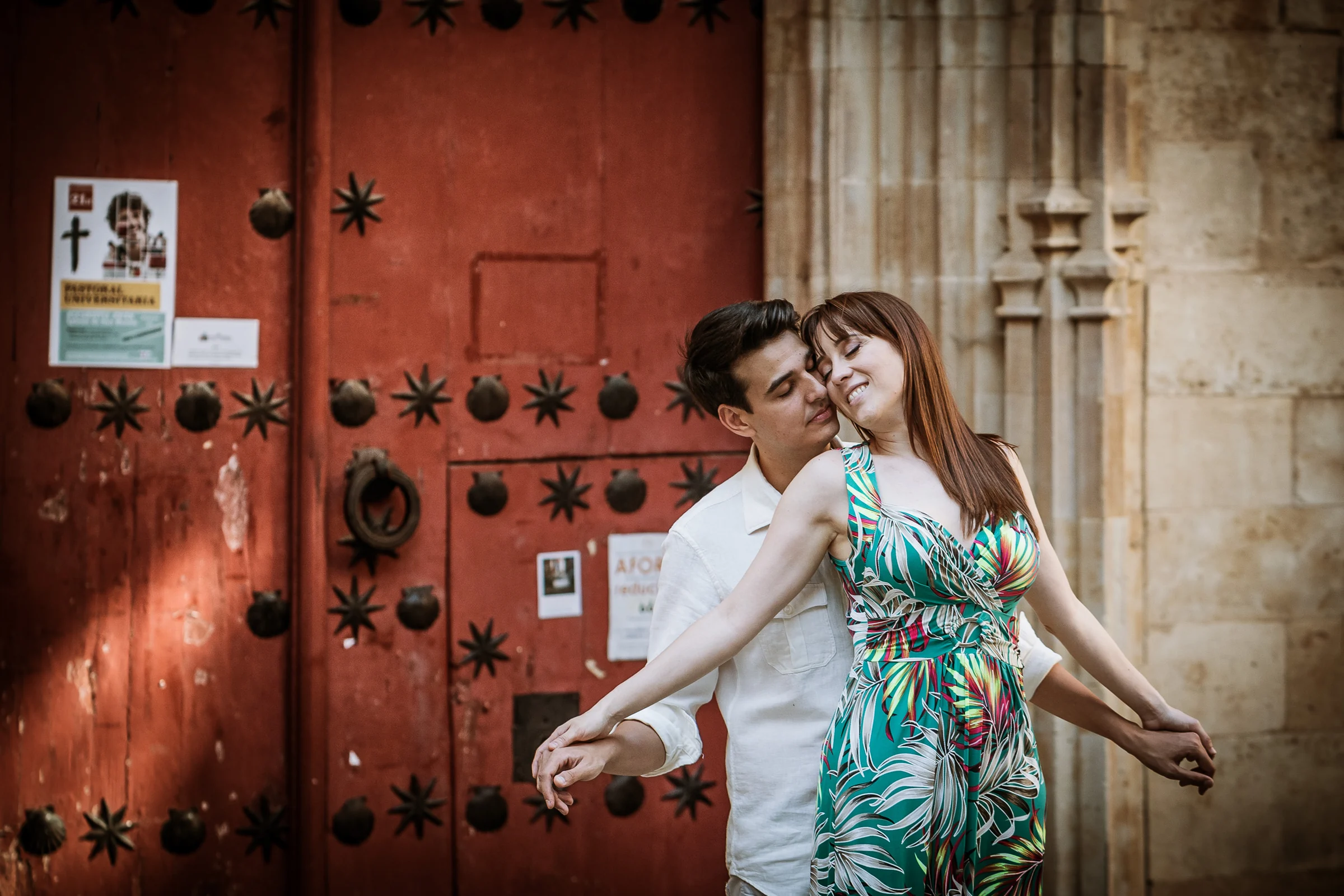 David y Noelia posan frente a una gran puerta roja de un edificio histórico de Salamanca.