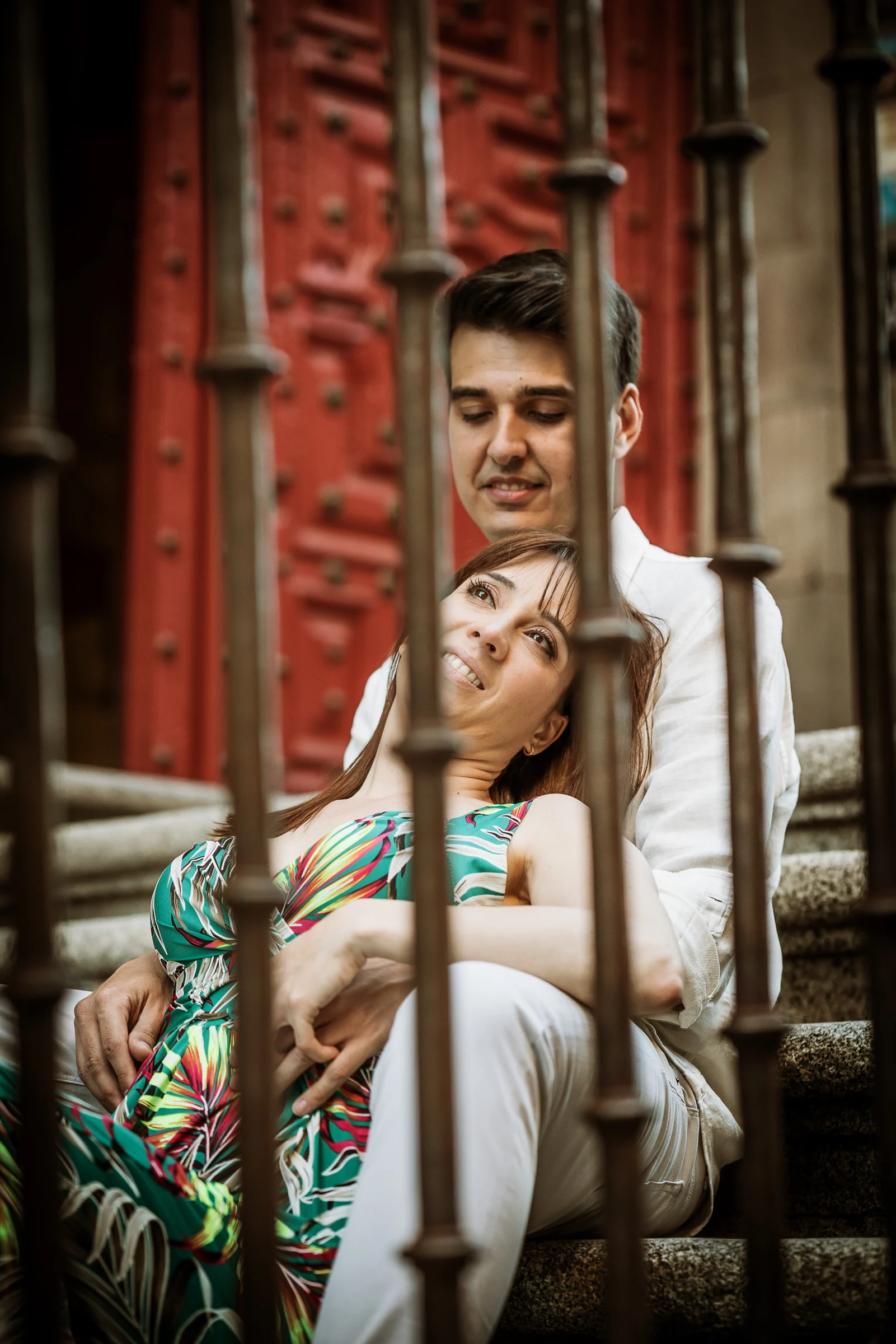 David y Noelia se abrazan junto a una puerta roja de piedra en una fotografía vertical de su preboda en Salamanca.