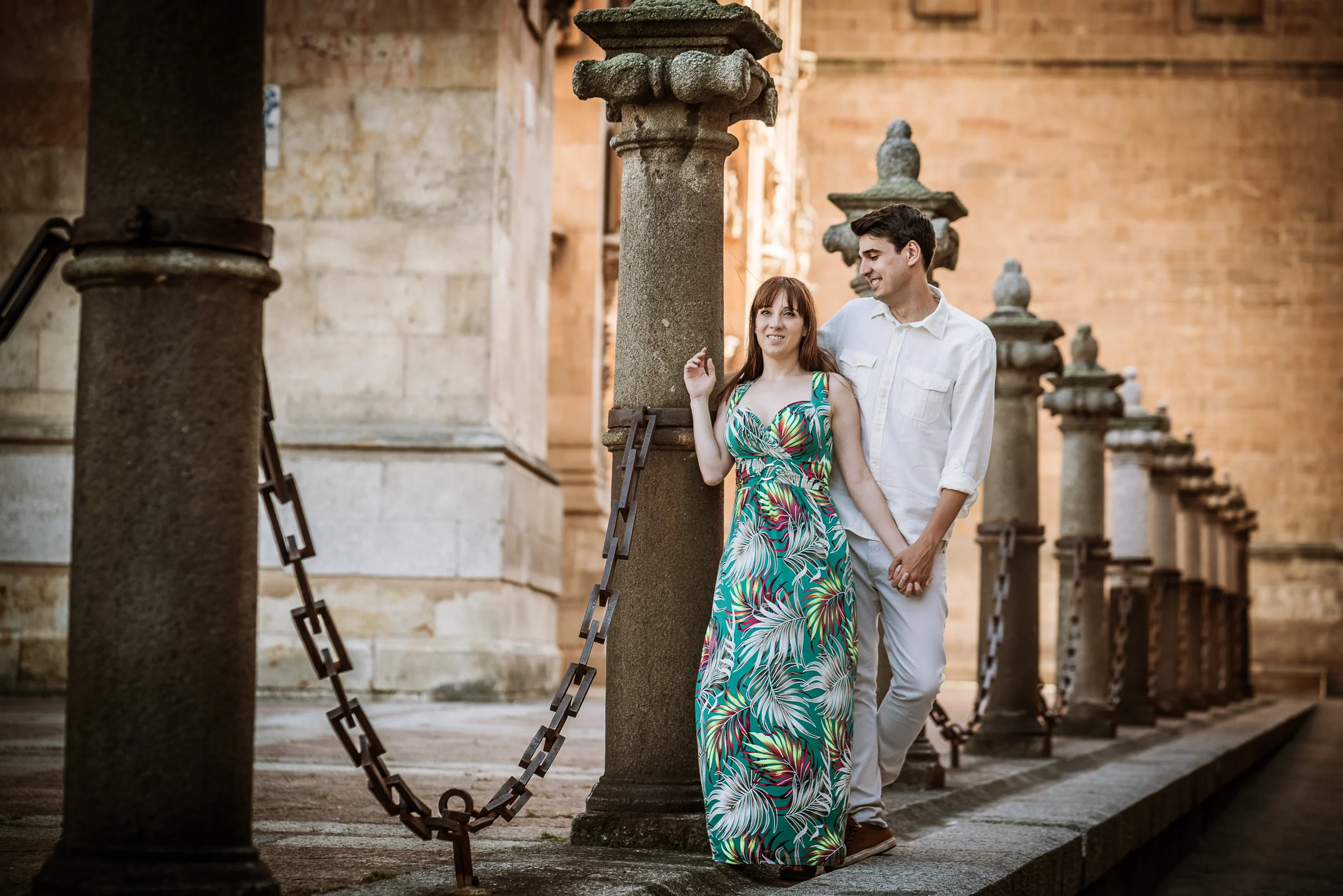 David y Noelia caminan entre columnas y cadenas en el entorno monumental de la Universidad de Salamanca.
