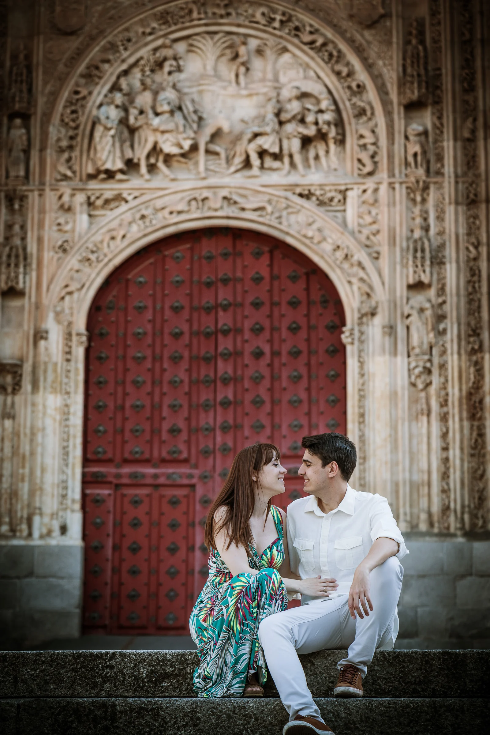 David y Noelia se sientan junto a una portada de piedra tallada durante su preboda en Salamanca.