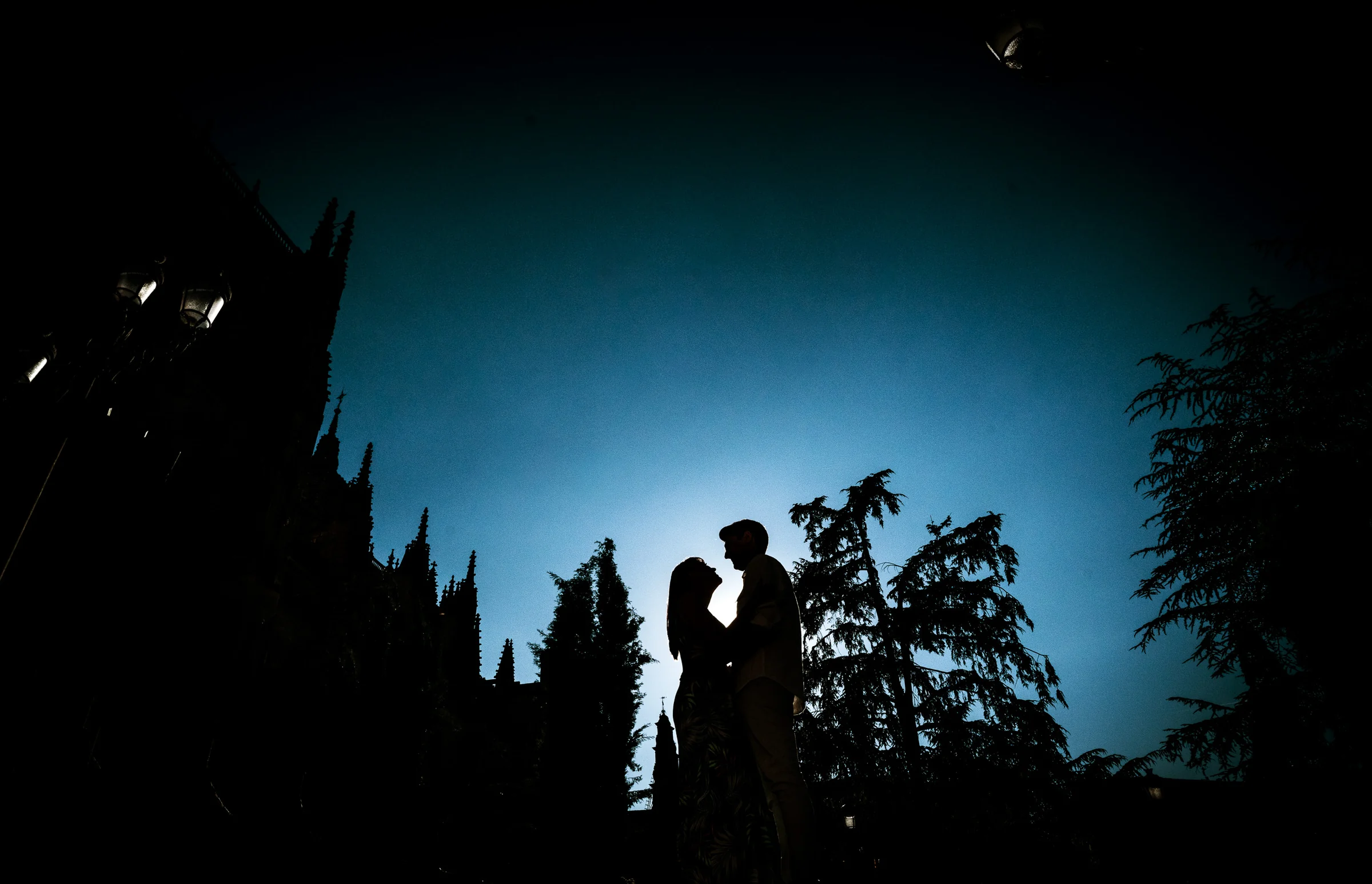 Silueta de David y Noelia entre árboles durante su preboda en los jardines del centro histórico de Salamanca.
