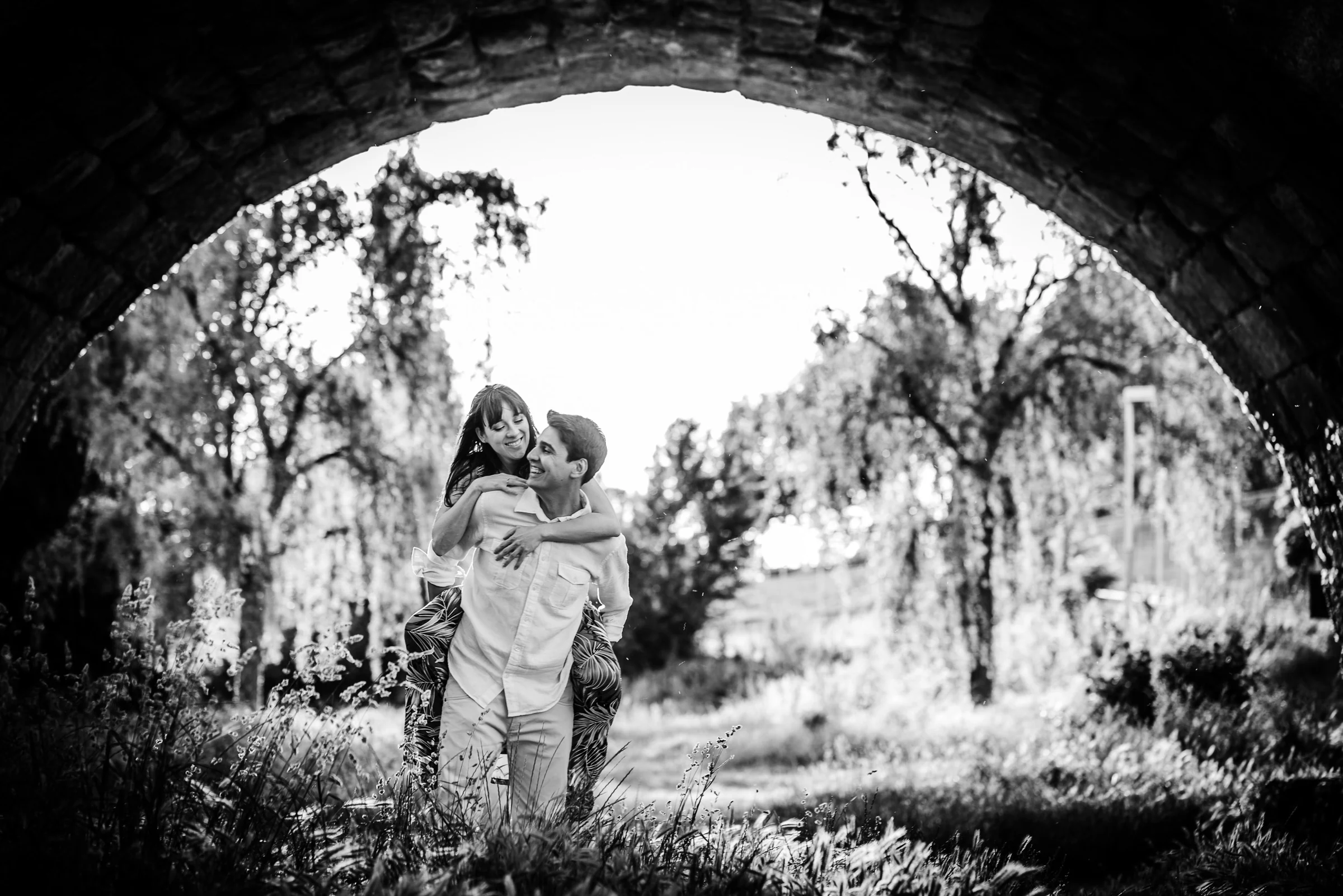 David y Noelia se abrazan en blanco y negro bajo un arco del Puente Romano de Salamanca.