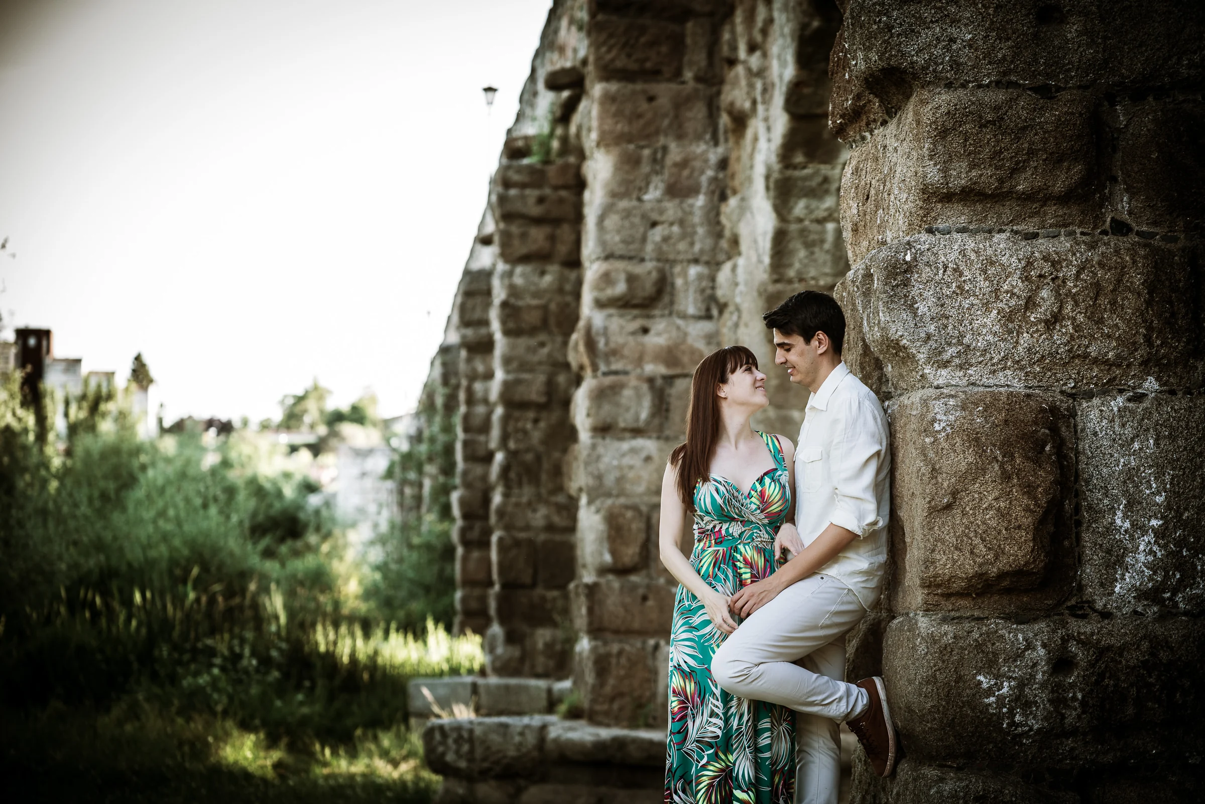 David y Noelia posan junto a un pilar de piedra del Puente Romano durante su preboda en Salamanca.