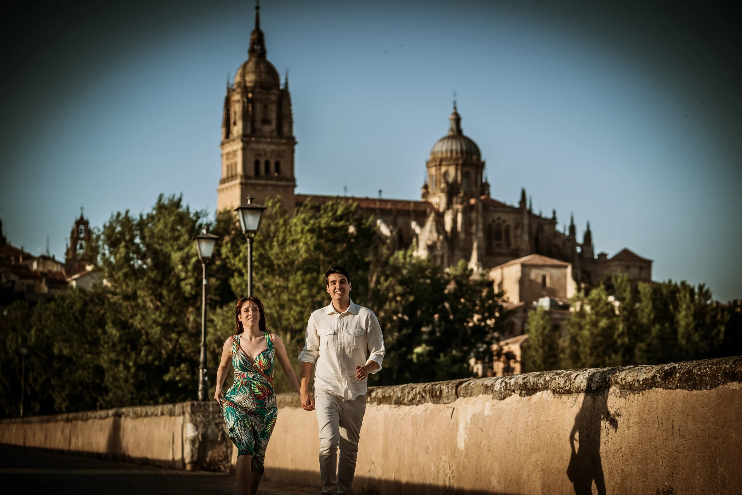 David y Noelia caminan por el Puente Romano con las catedrales de Salamanca al fondo durante su preboda.