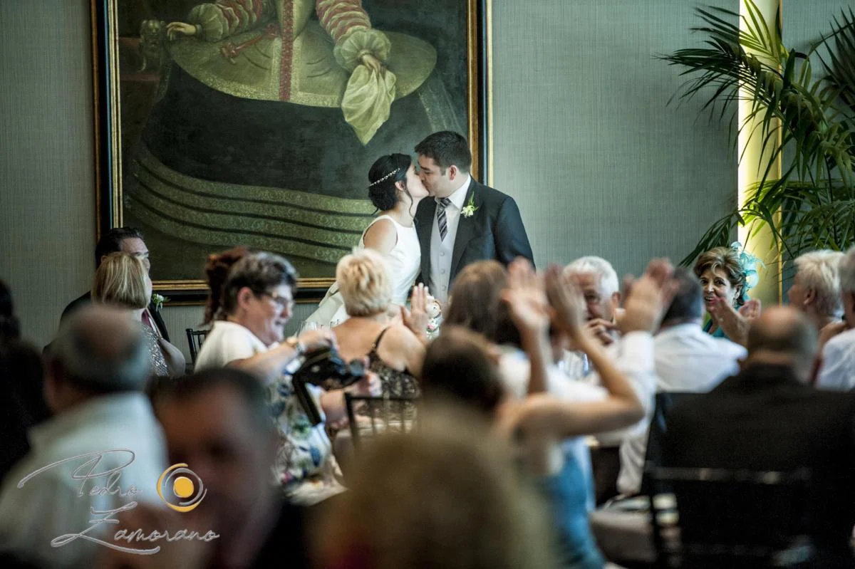 Novios besándose durante la celebración rodeados de invitados que aplauden.