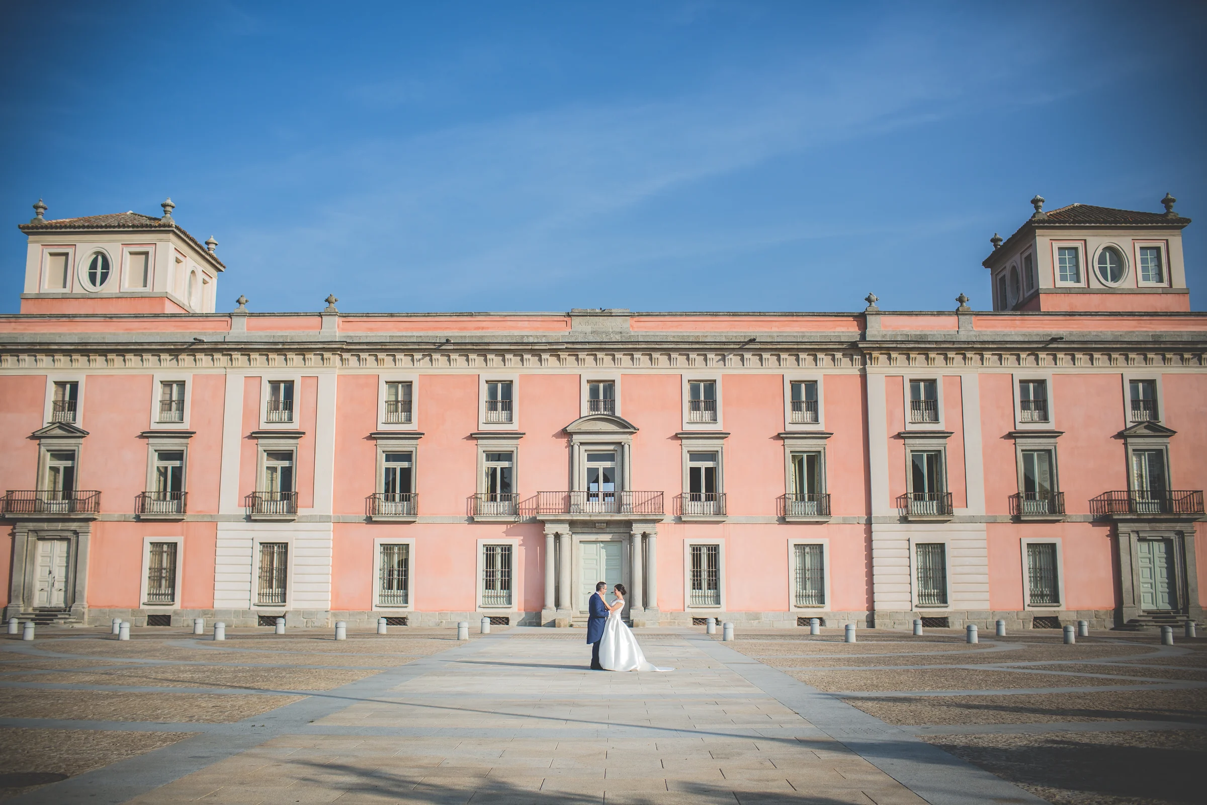 Pareja de novios muy pequeña frente a la gran fachada del palacio de Boadilla del Monte.