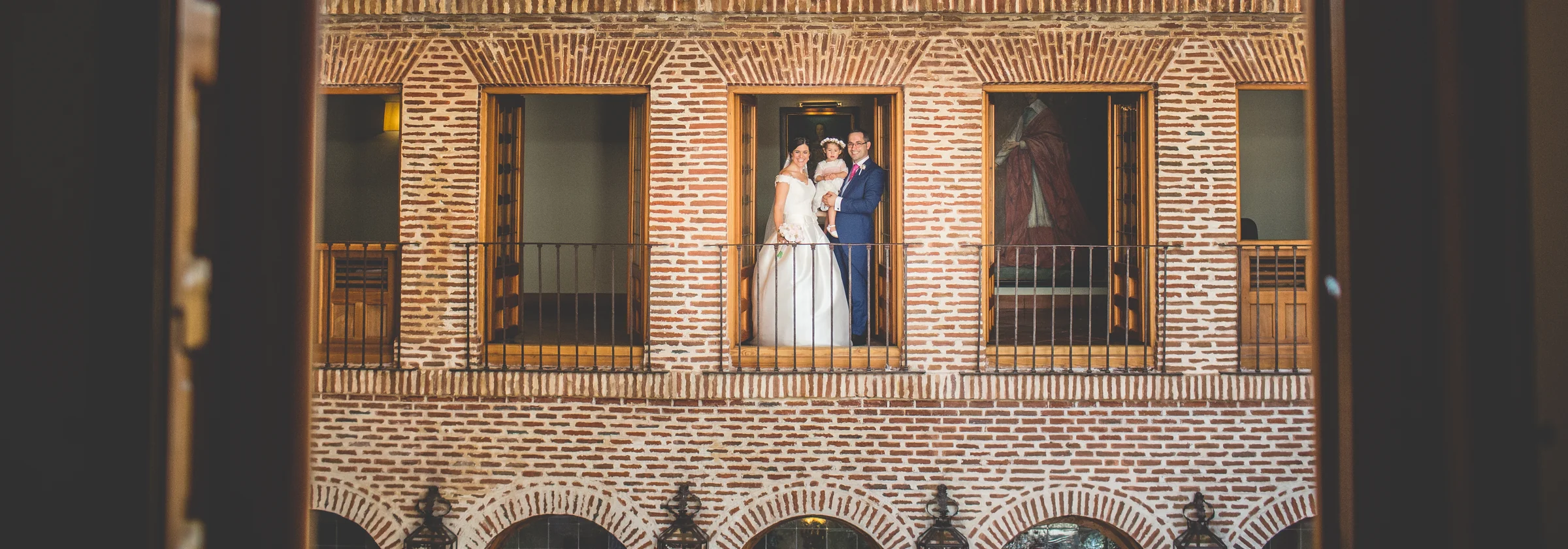 Pareja con una niña en brazos posando en el balcón del patio de ladrillo.