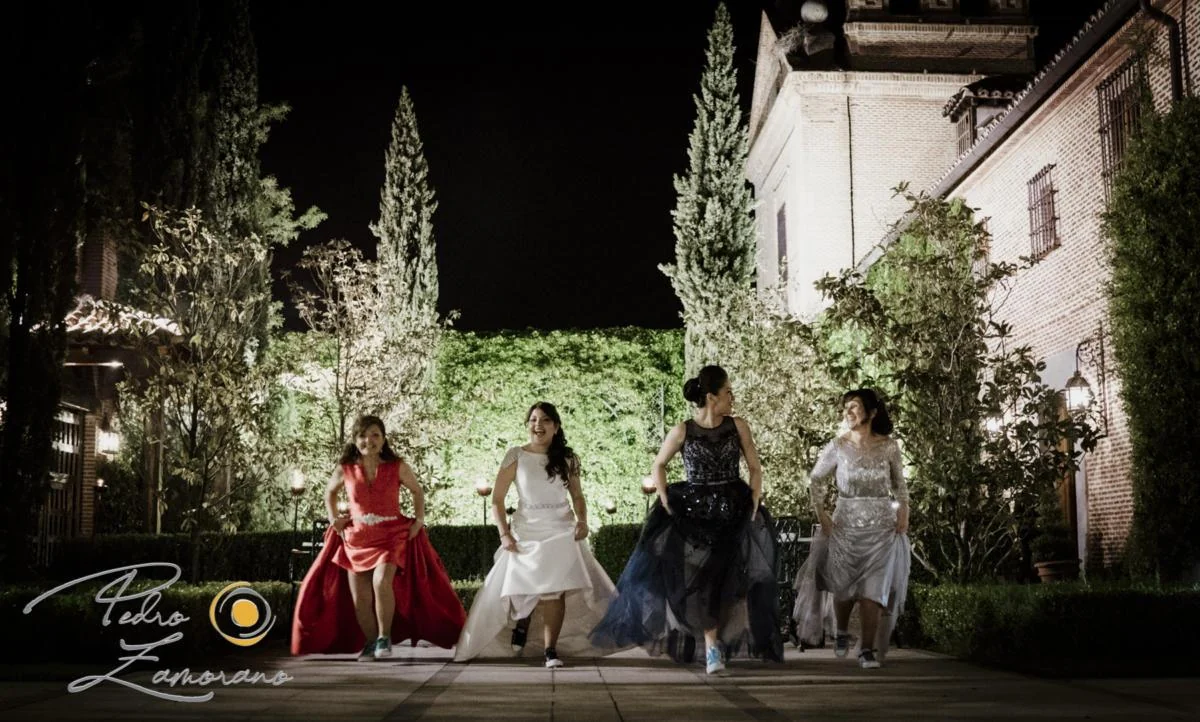 Novia caminando de noche con varias acompañantes en los jardines del recinto.