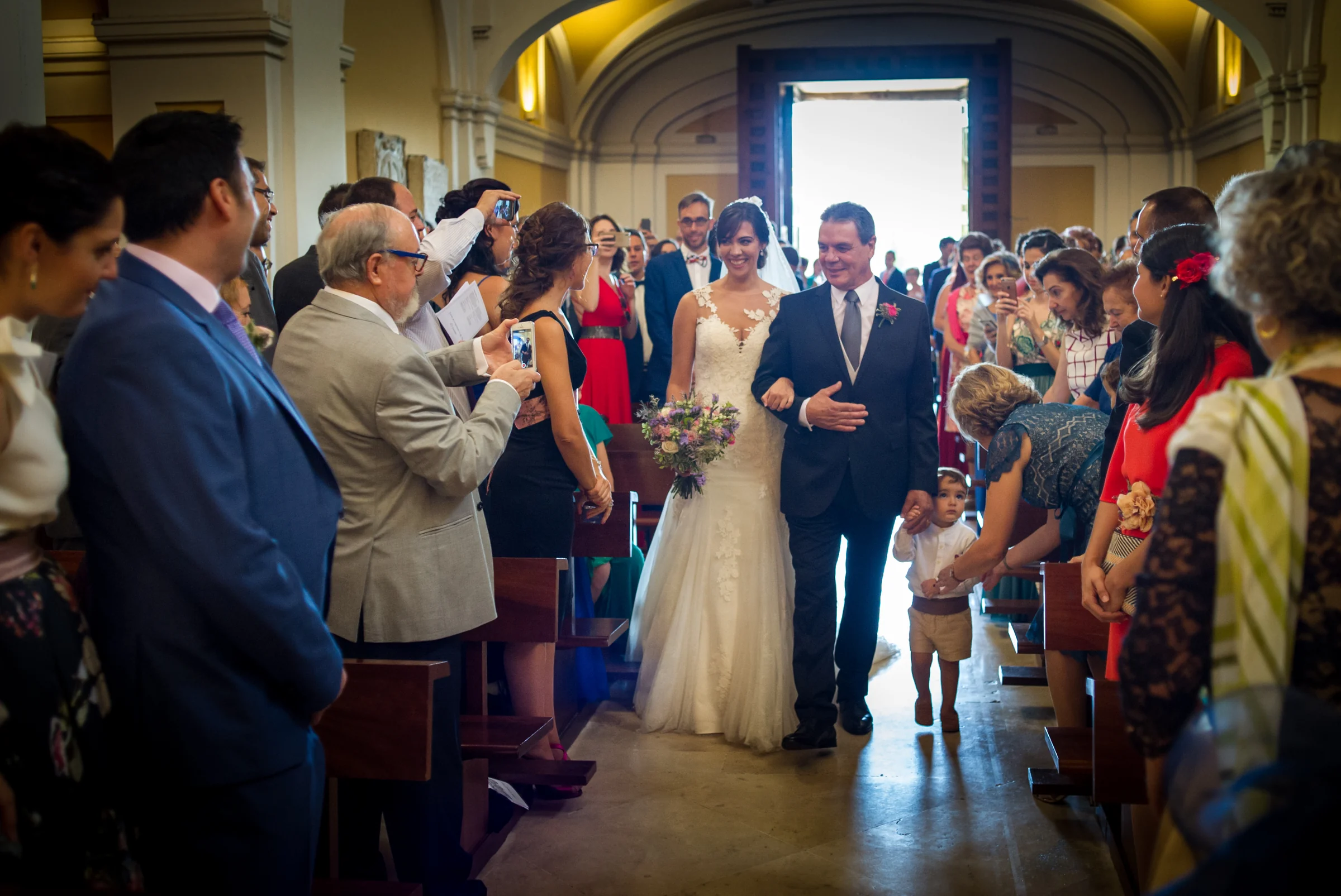 Novia entrando en la ceremonia del brazo de su padre mientras los invitados miran.