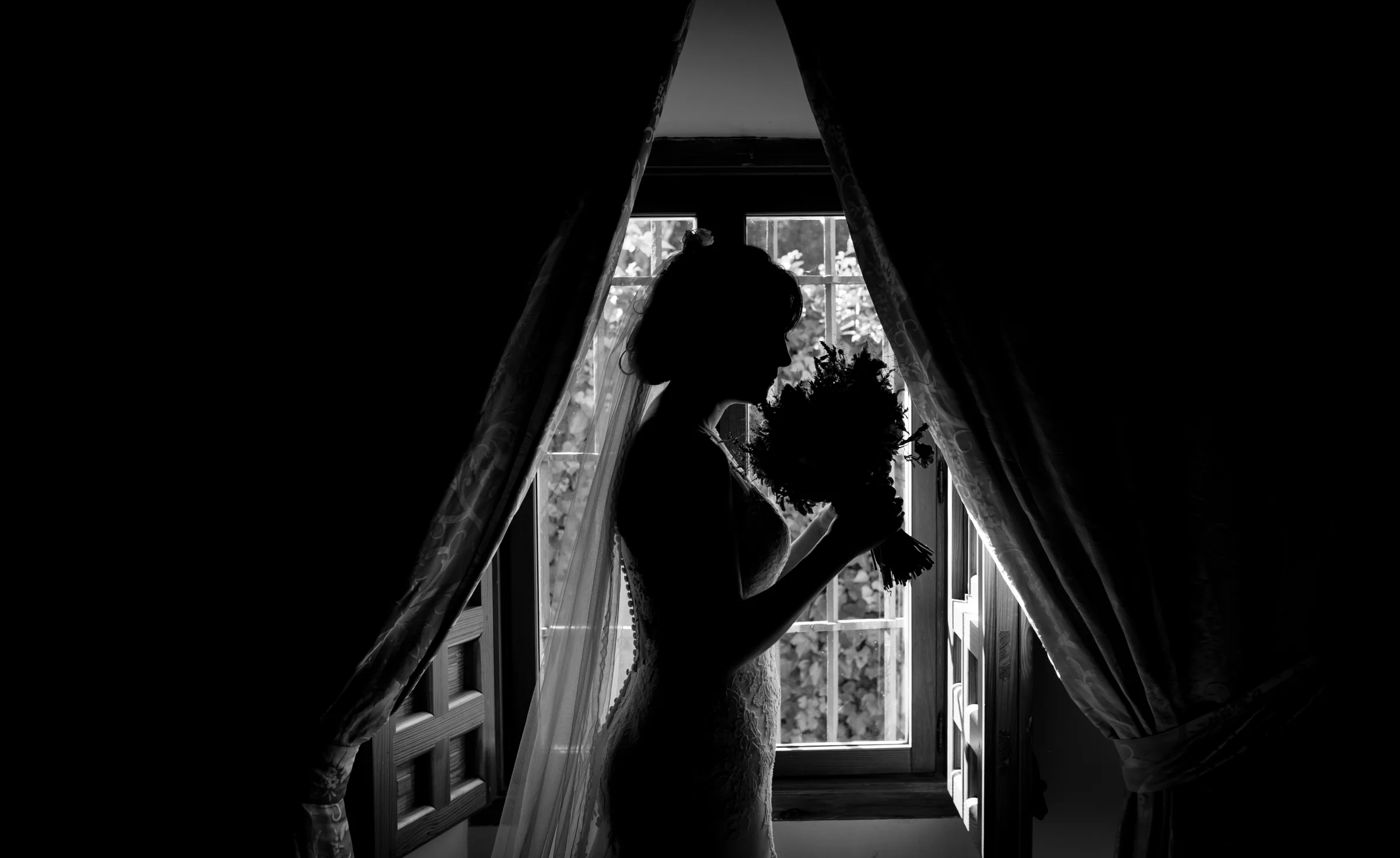 Silueta en blanco y negro de una novia sosteniendo su ramo frente a una ventana.