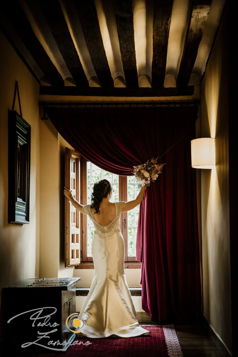 Novia junto a la ventana y las cortinas durante los preparativos de su boda.