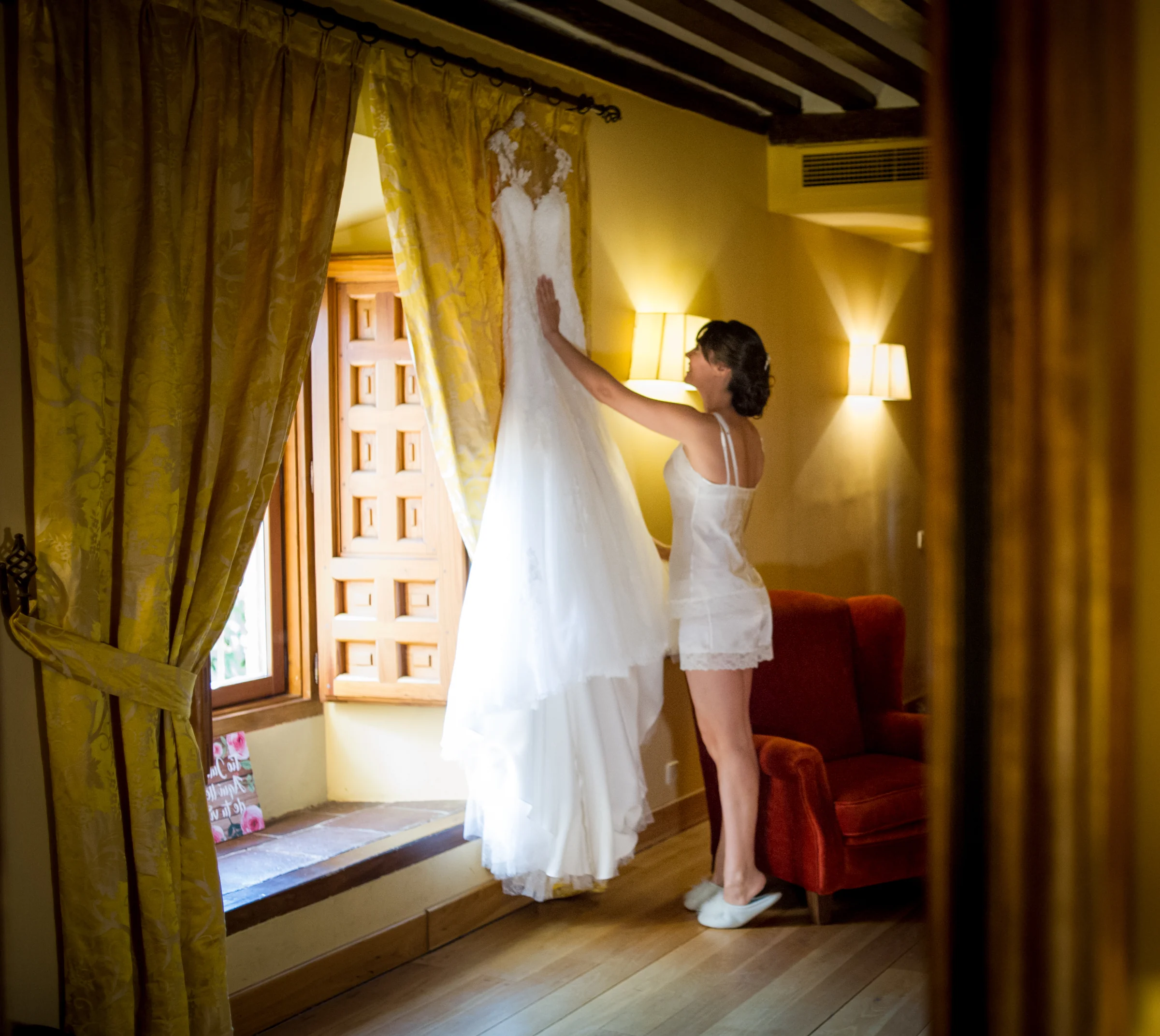 Novia levantando su vestido junto a una ventana durante los preparativos.