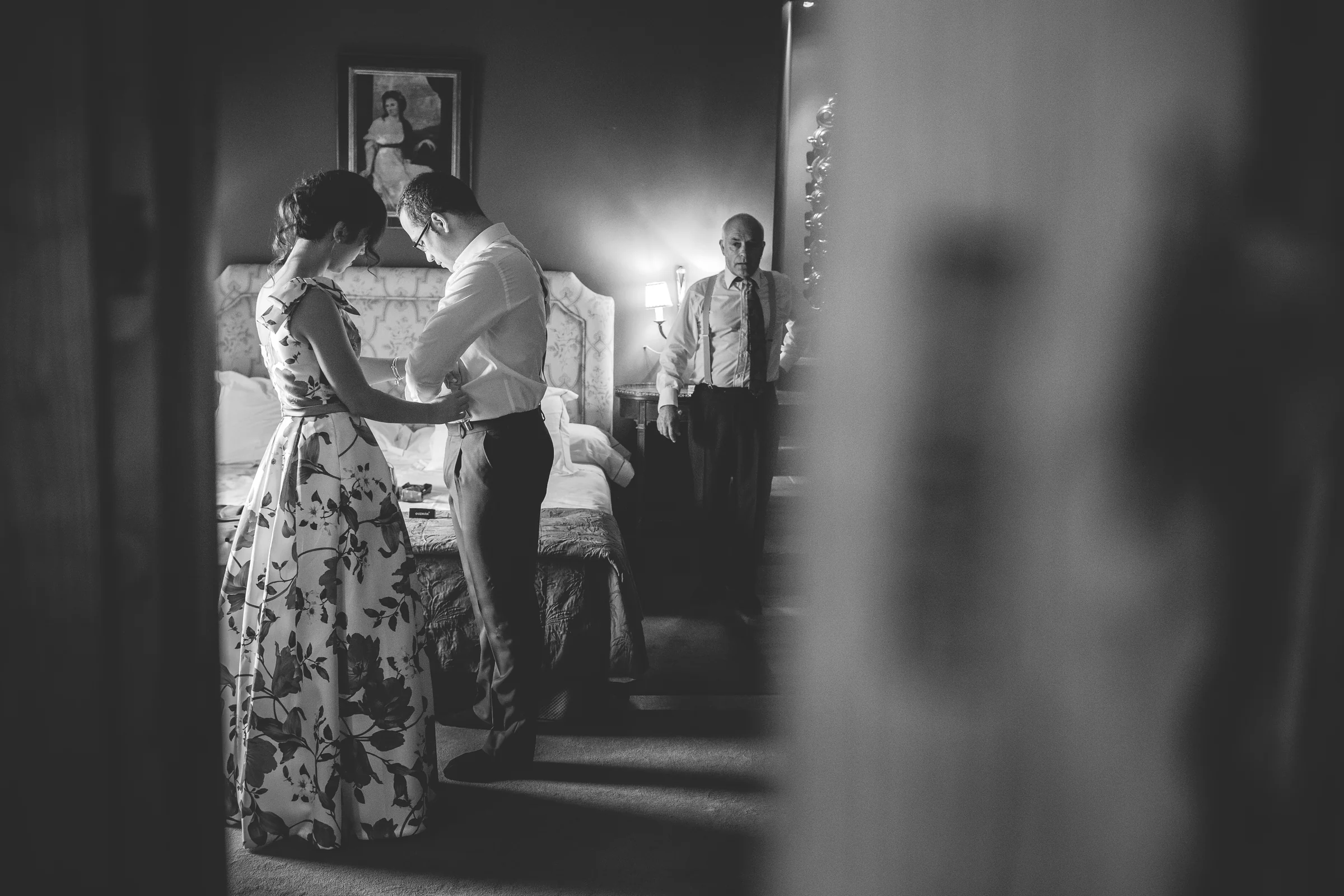 Acompañante ayudando al novio a vestirse en una fotografía en blanco y negro.